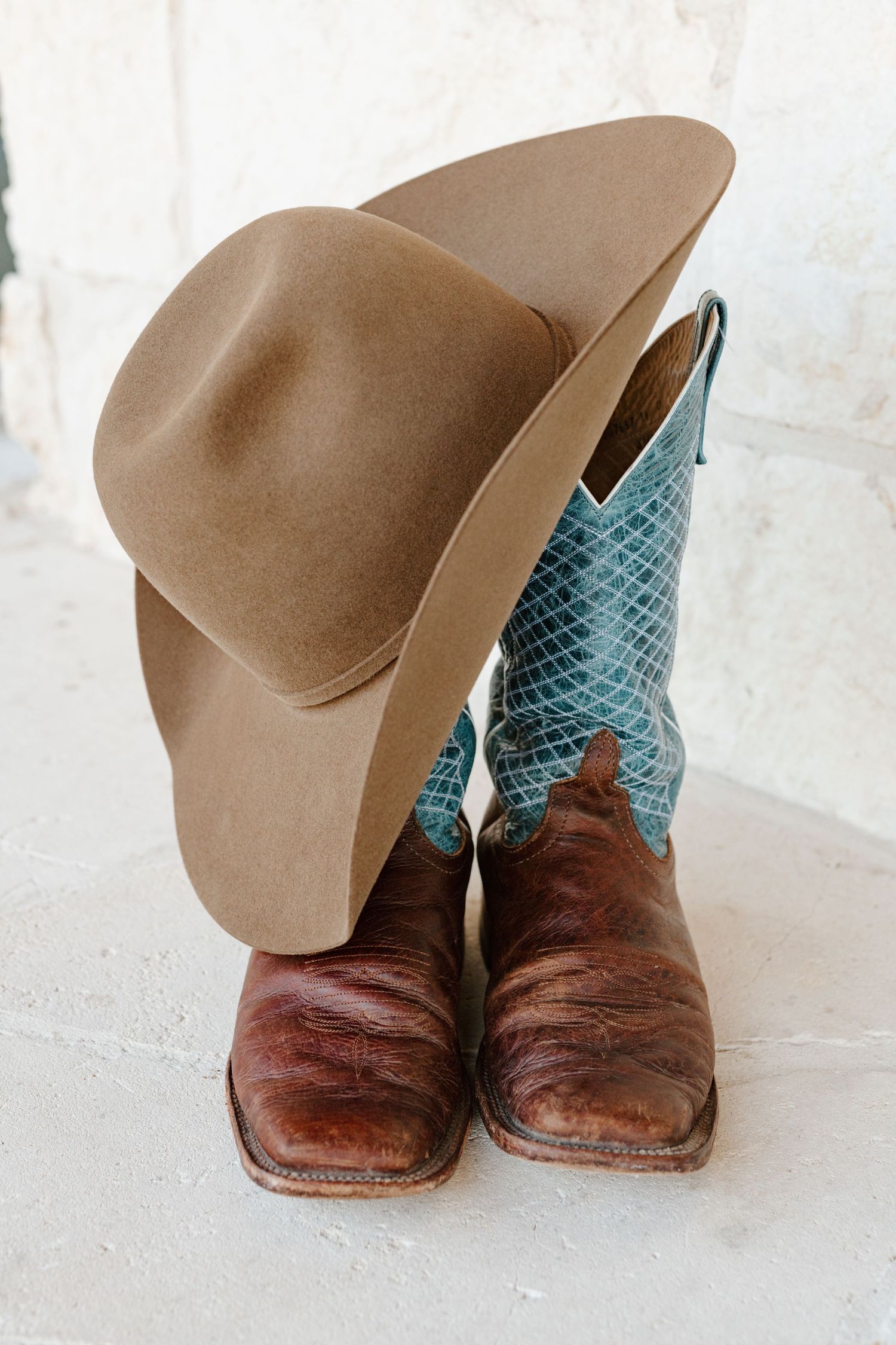 A tan cowboy hat rests on top of brown leather western boots with turquoise snakeskin pattern shafts.