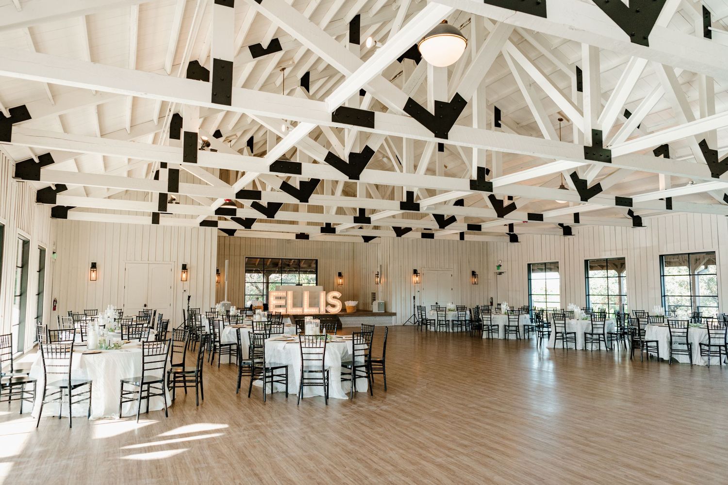 Elegant white reception hall with vaulted ceiling, decorative black lanterns, and chiavari chairs arranged for an event.