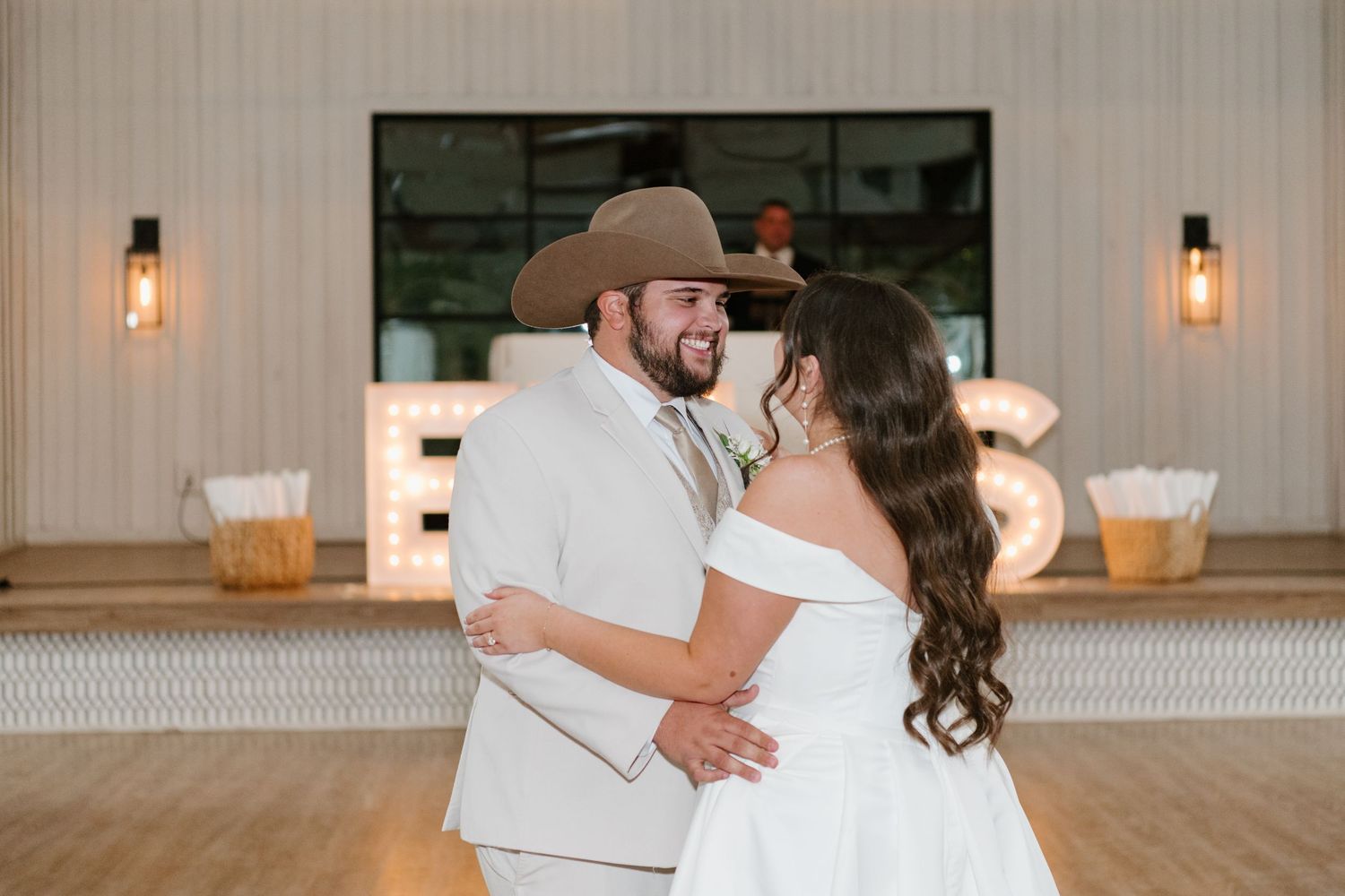A couple shares their first dance together in a rustic reception venue with wall sconces and a wooden bar.