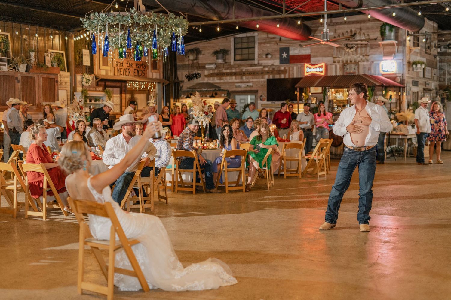 Wedding reception dance scene with guests in rustic barn venue with string lights.