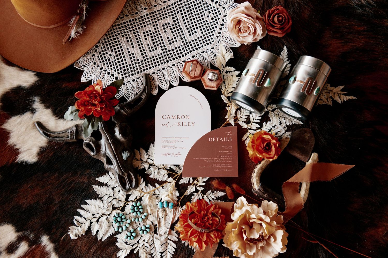 Wedding stationery and decorative elements with lace doily and flowers on cowhide background.
