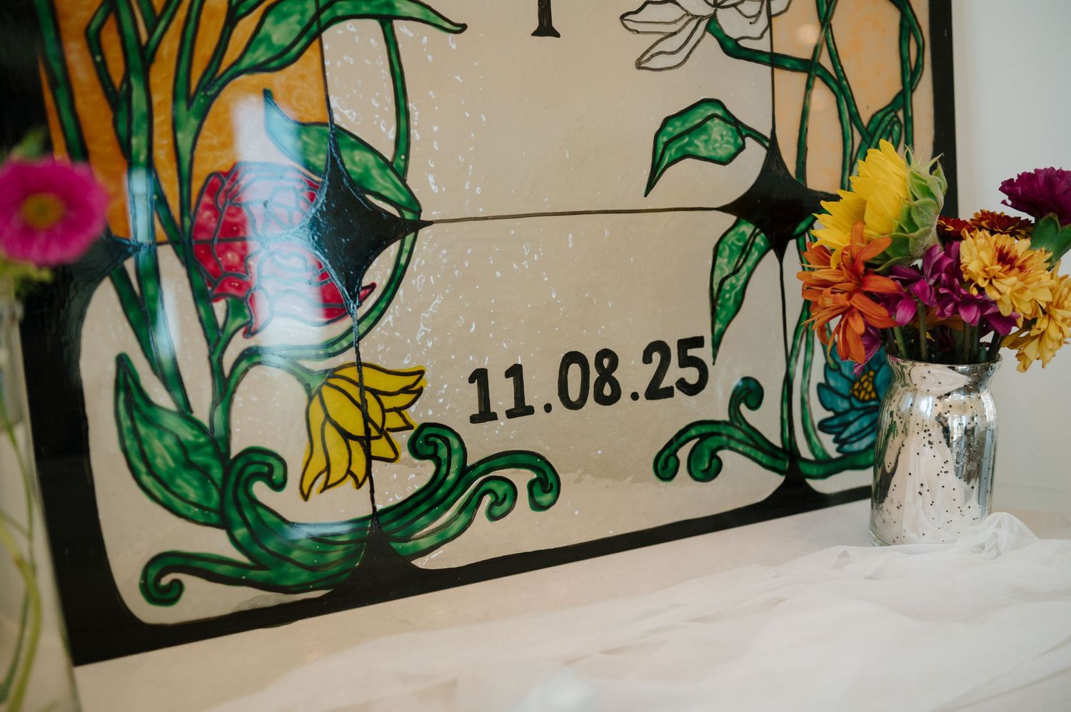 A decorative framed date display with floral designs and a small vase of colorful flowers beside it.