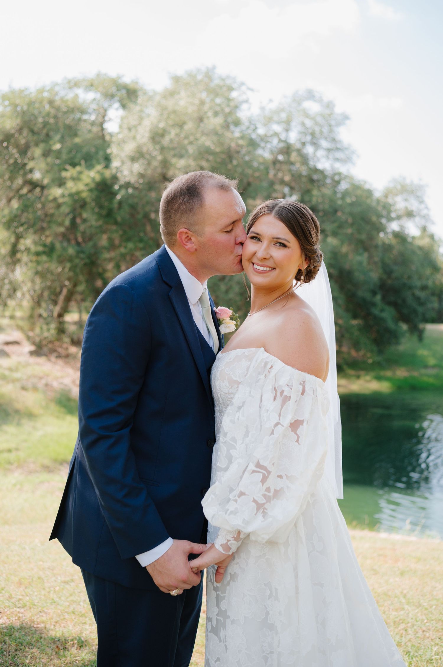 Couple shares intimate moment during outdoor wedding photoshoot by a pond.