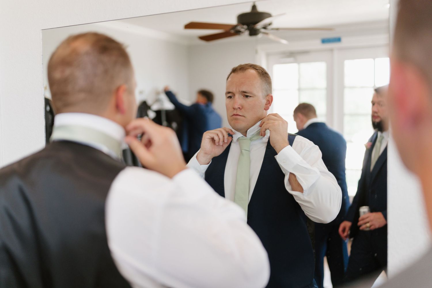 Wedding guests in formal attire gather in a bright indoor venue.
