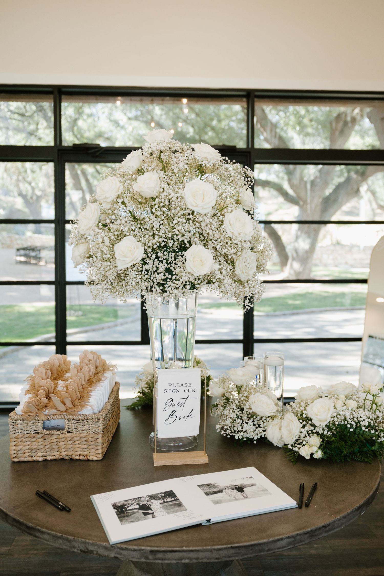Elegant wedding guest book table with white rose centerpiece, baby's breath arrangement and woven basket of bread.