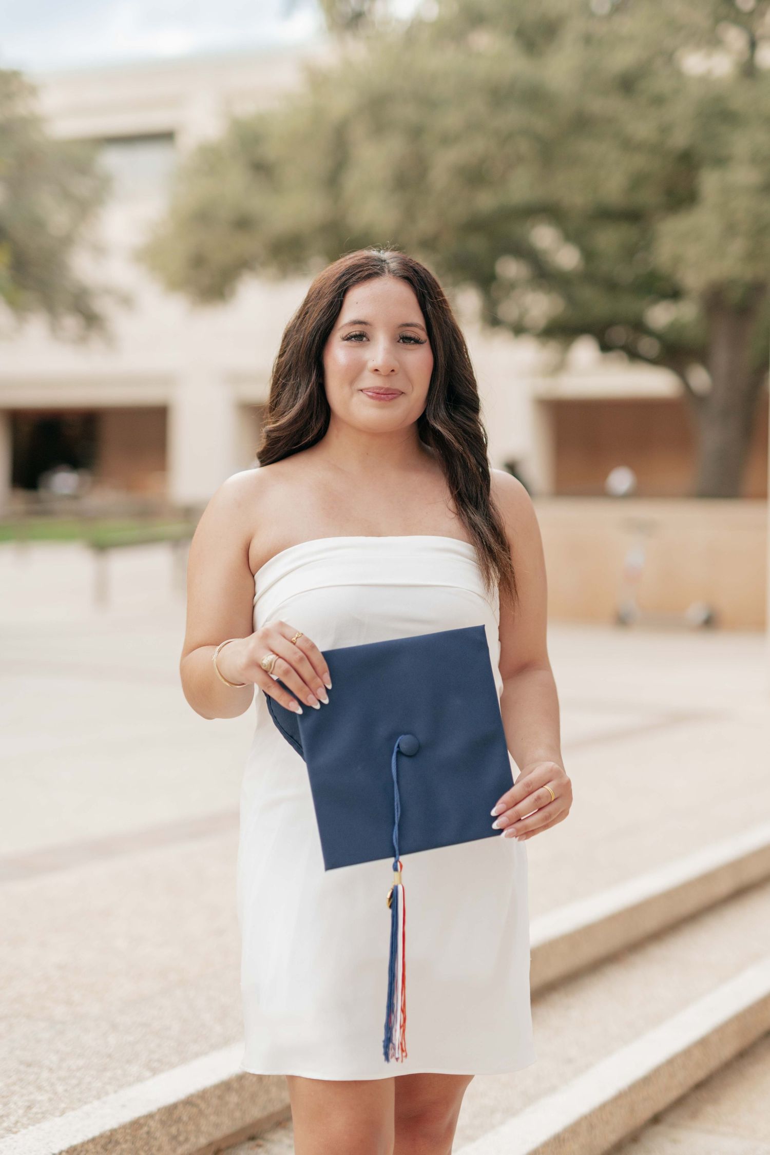 Graduate holds diploma while posing in white dress for graduation photos.