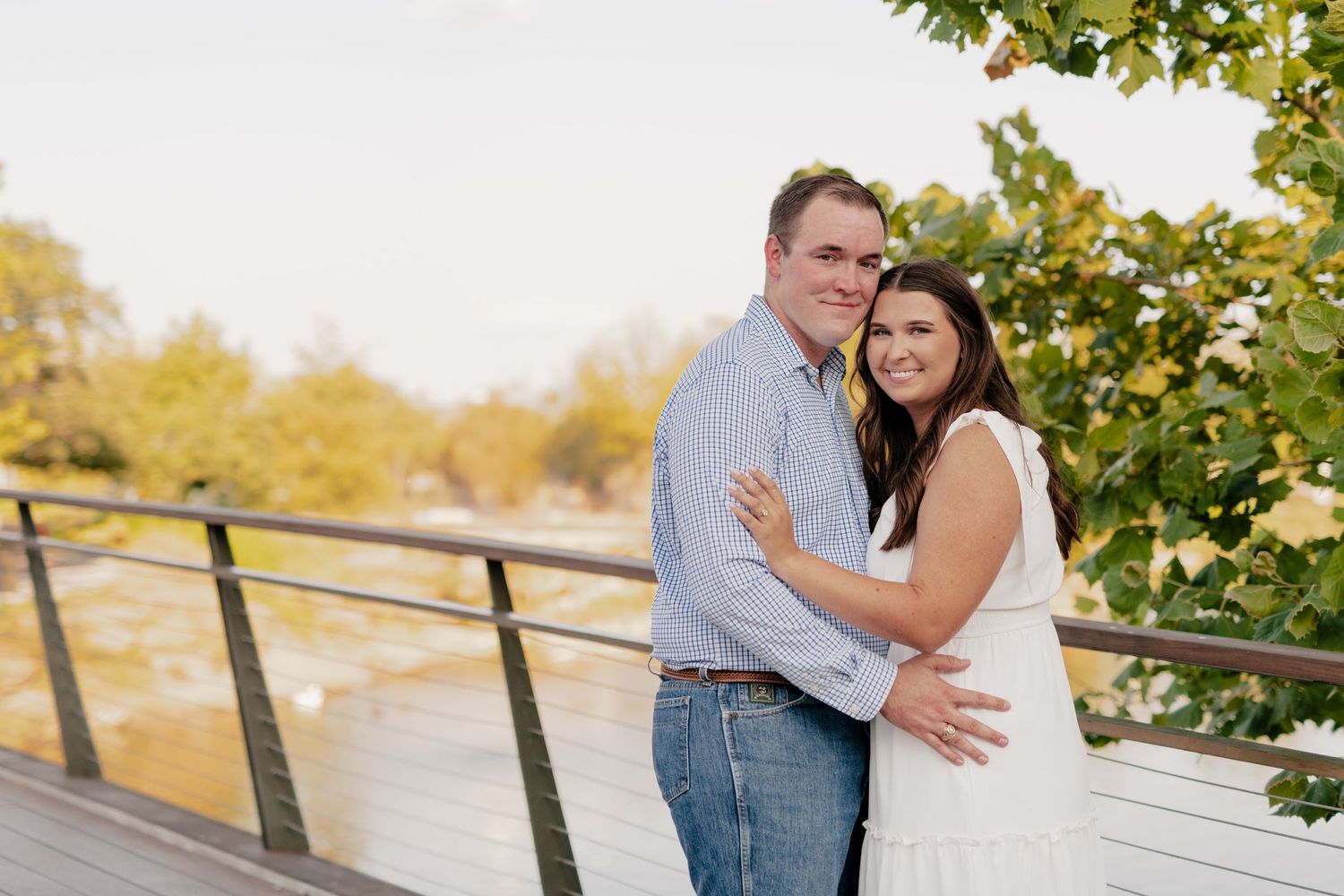 A couple embraces on a wooden deck surrounded by autumn foliage and golden sunlight.