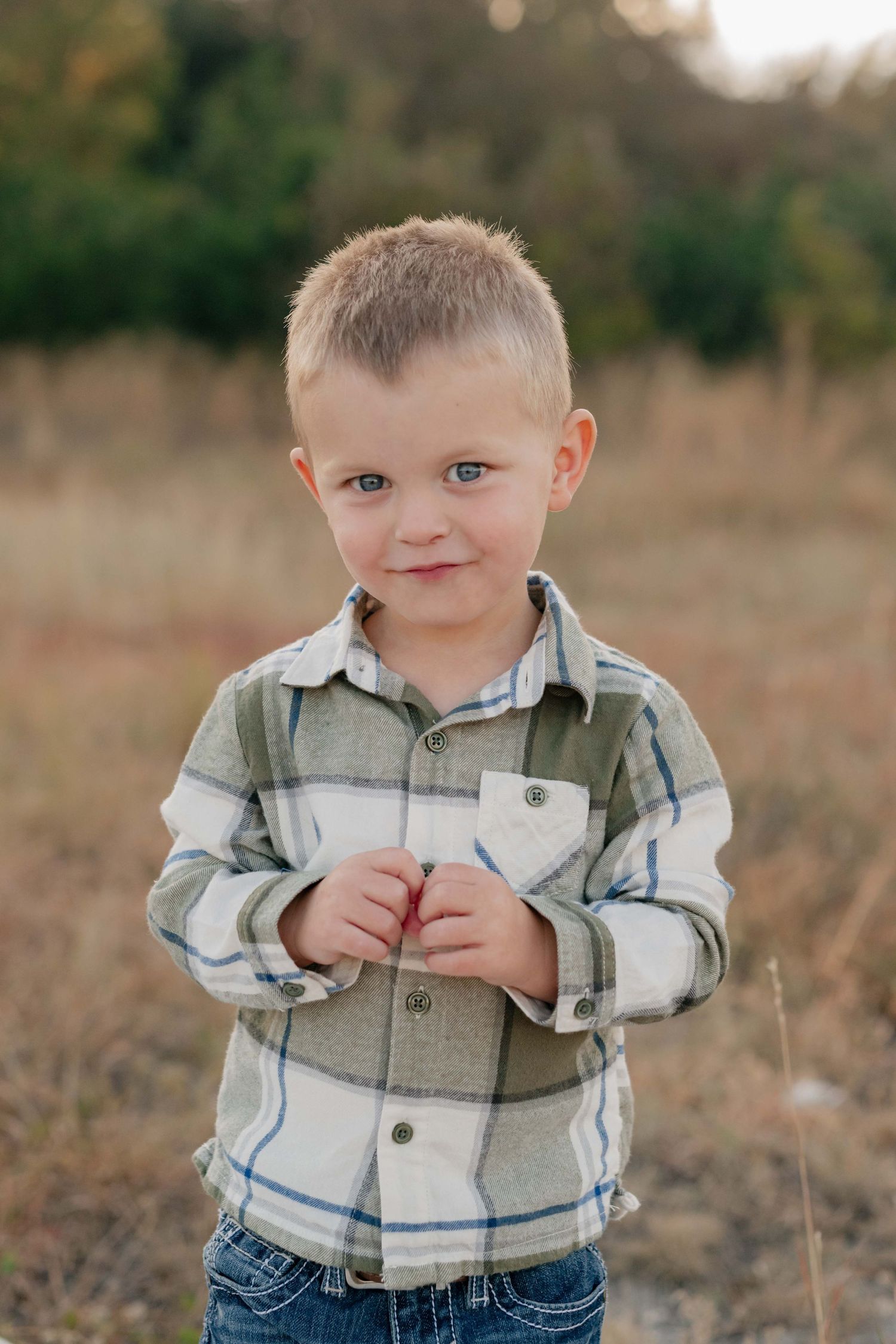 Young child in plaid shirt smiling while standing in autumn field.