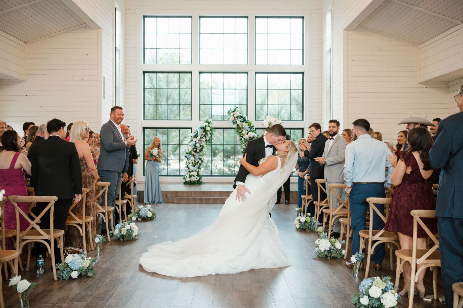A bride and groom embracing and kissing during their wedding ceremony, with guests seated in the background.
