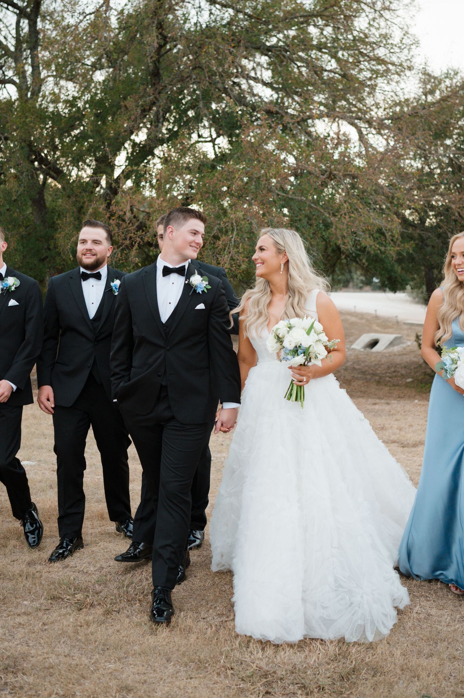 A bride and groom walking together on a path surrounded by trees.