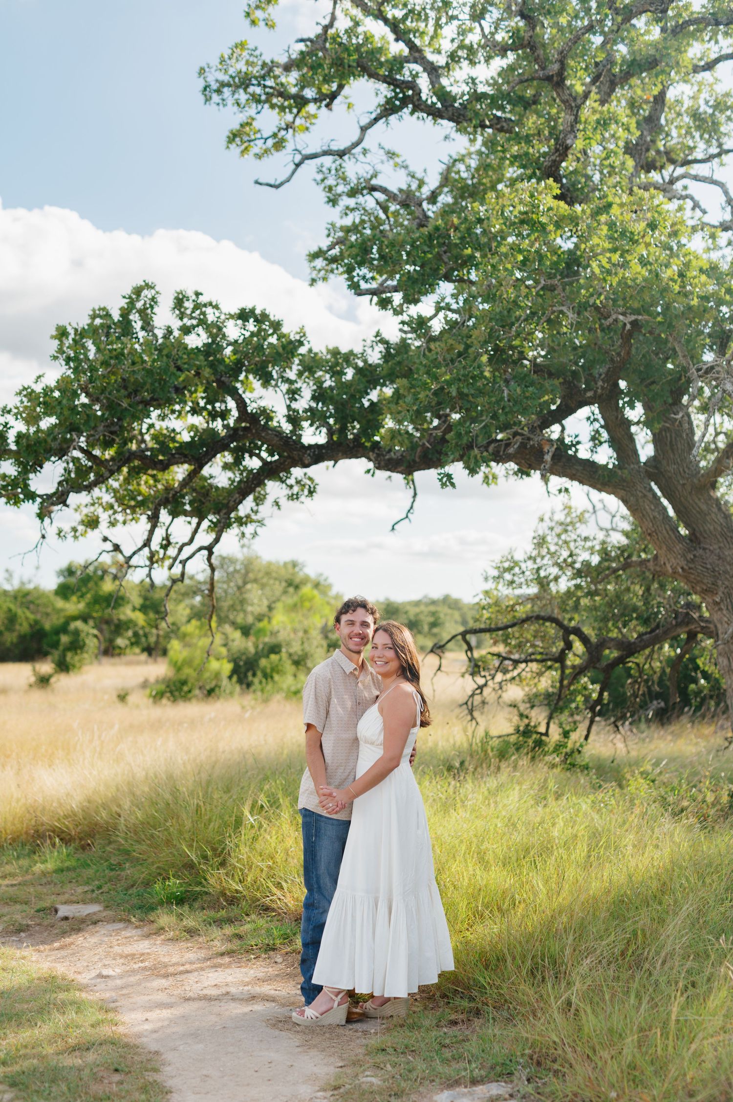 A couple shares intimate moments while walking along a nature trail surrounded by tall grass.