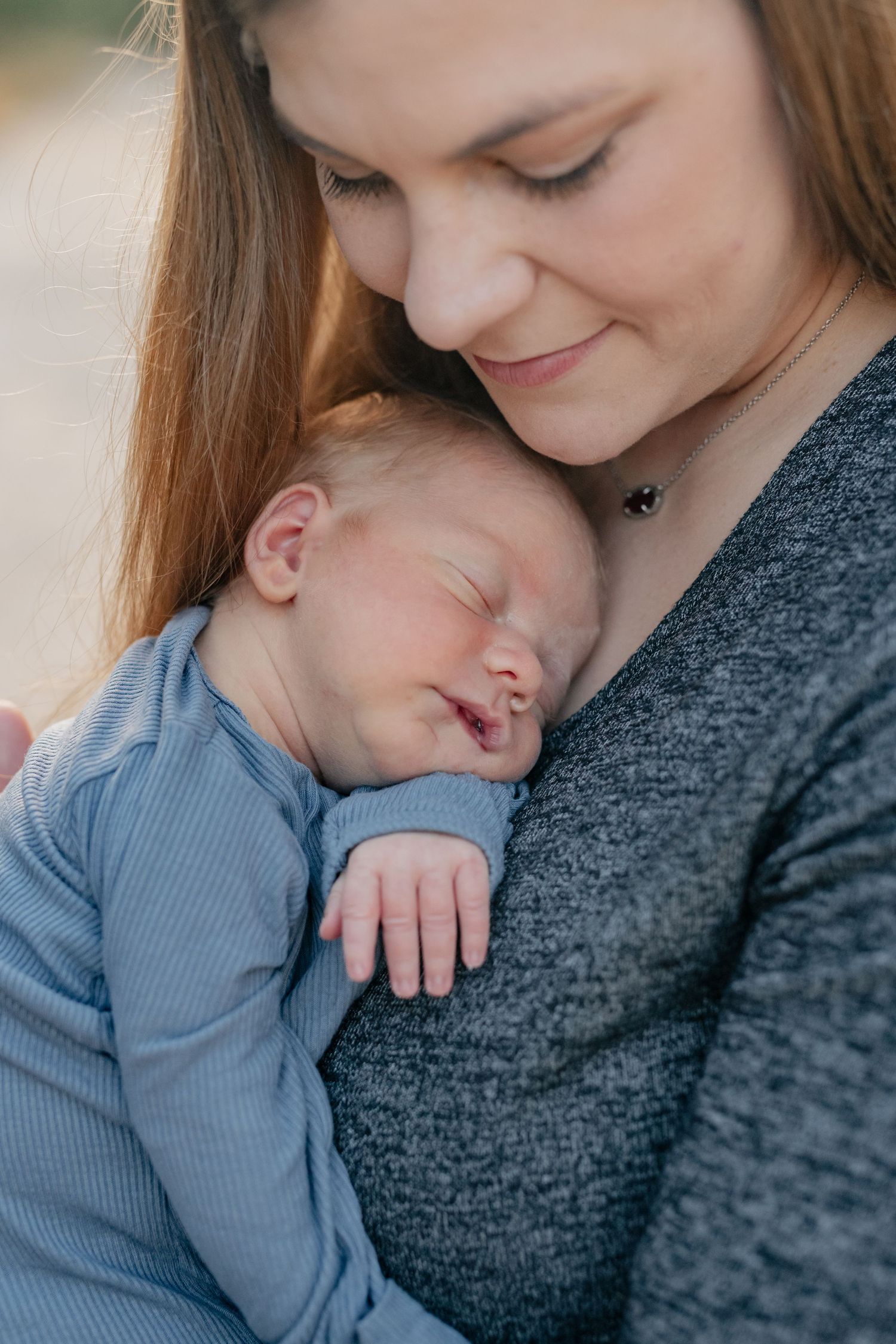 Peaceful moment as mother snuggles sleeping infant in blue wearing gray sweater.
