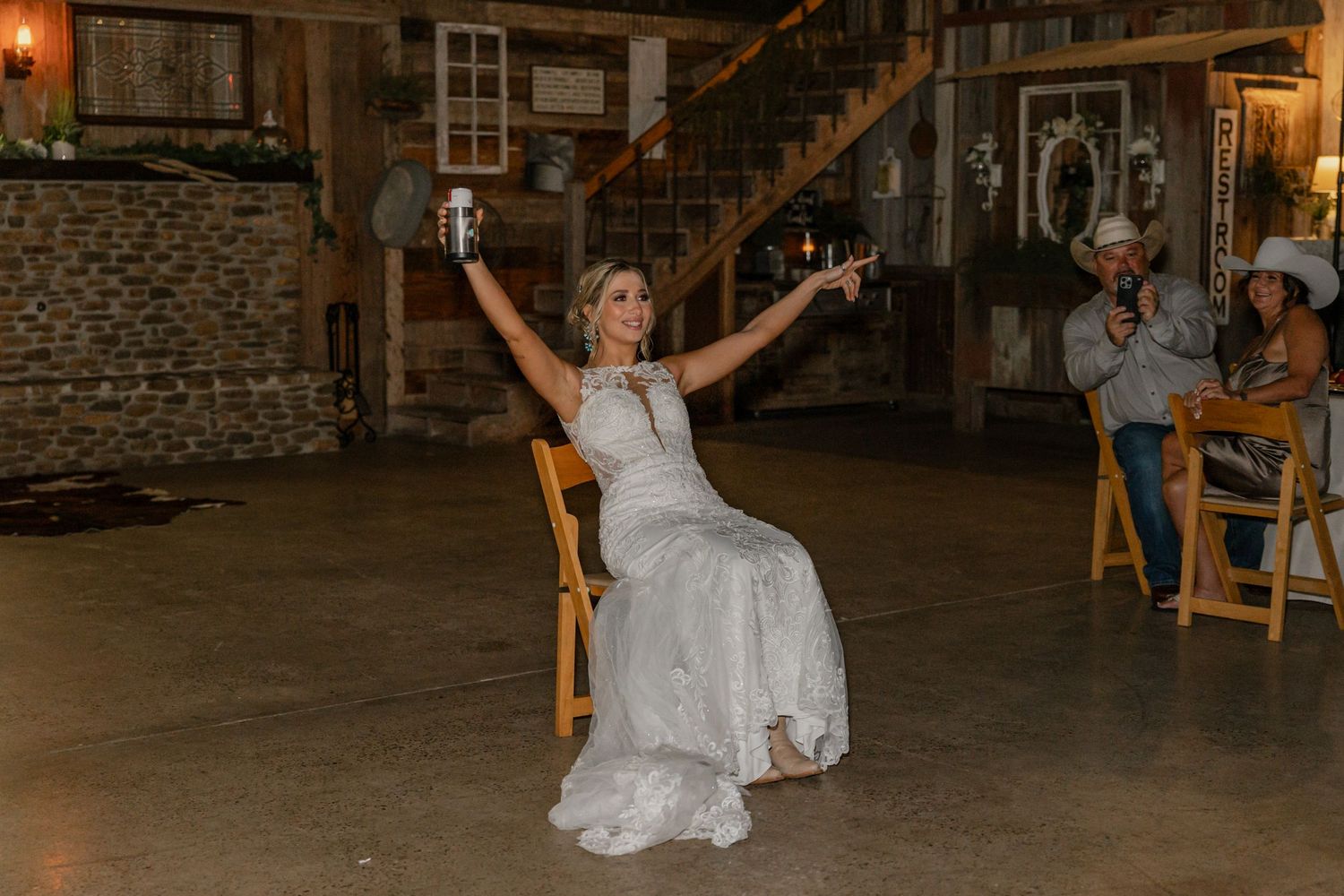 A bride celebrates joyfully in her white gown while seated in a rustic barn setting.