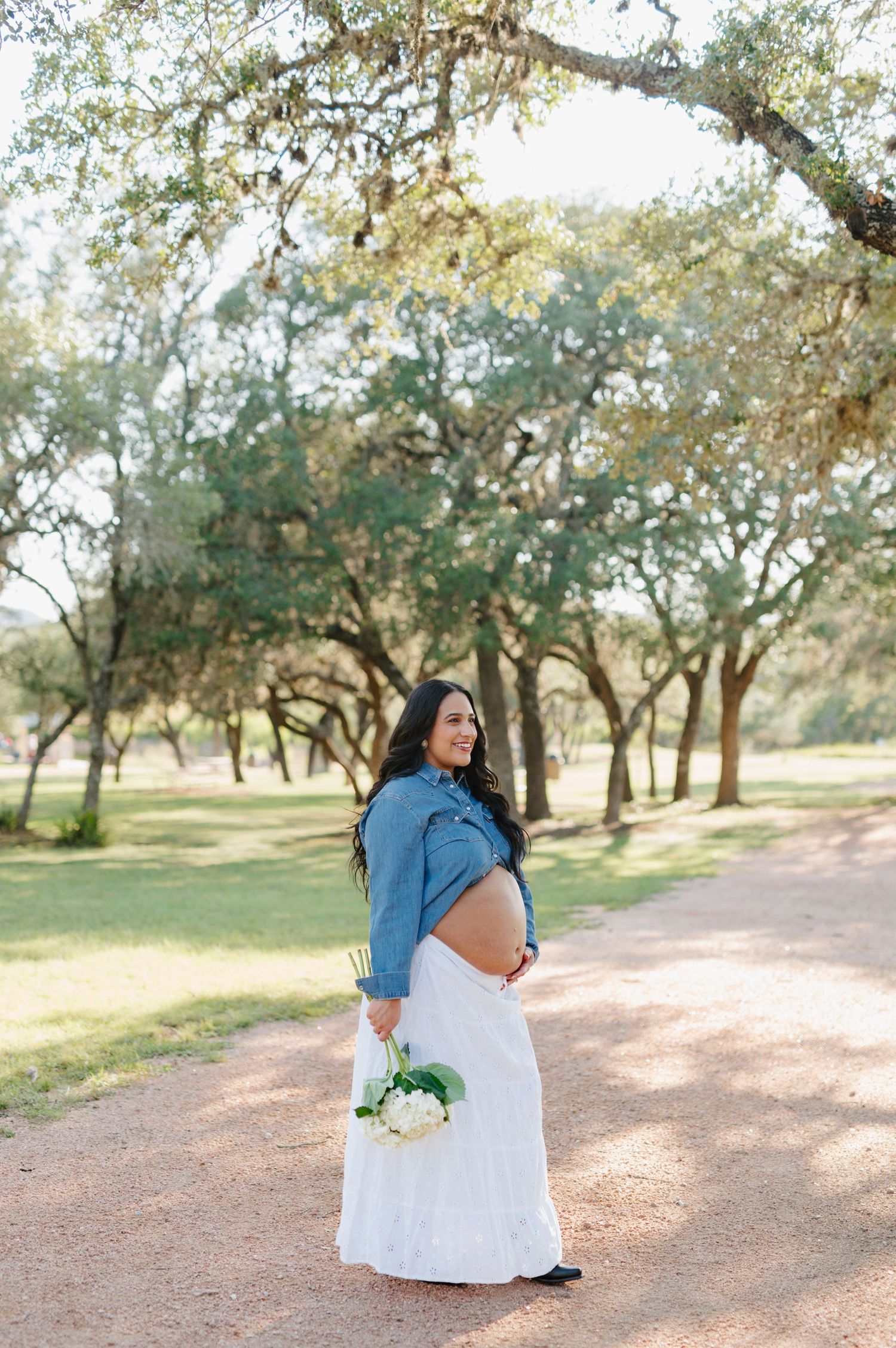 A romantic couple embraces on a dirt path under oak trees in a natural outdoor setting.