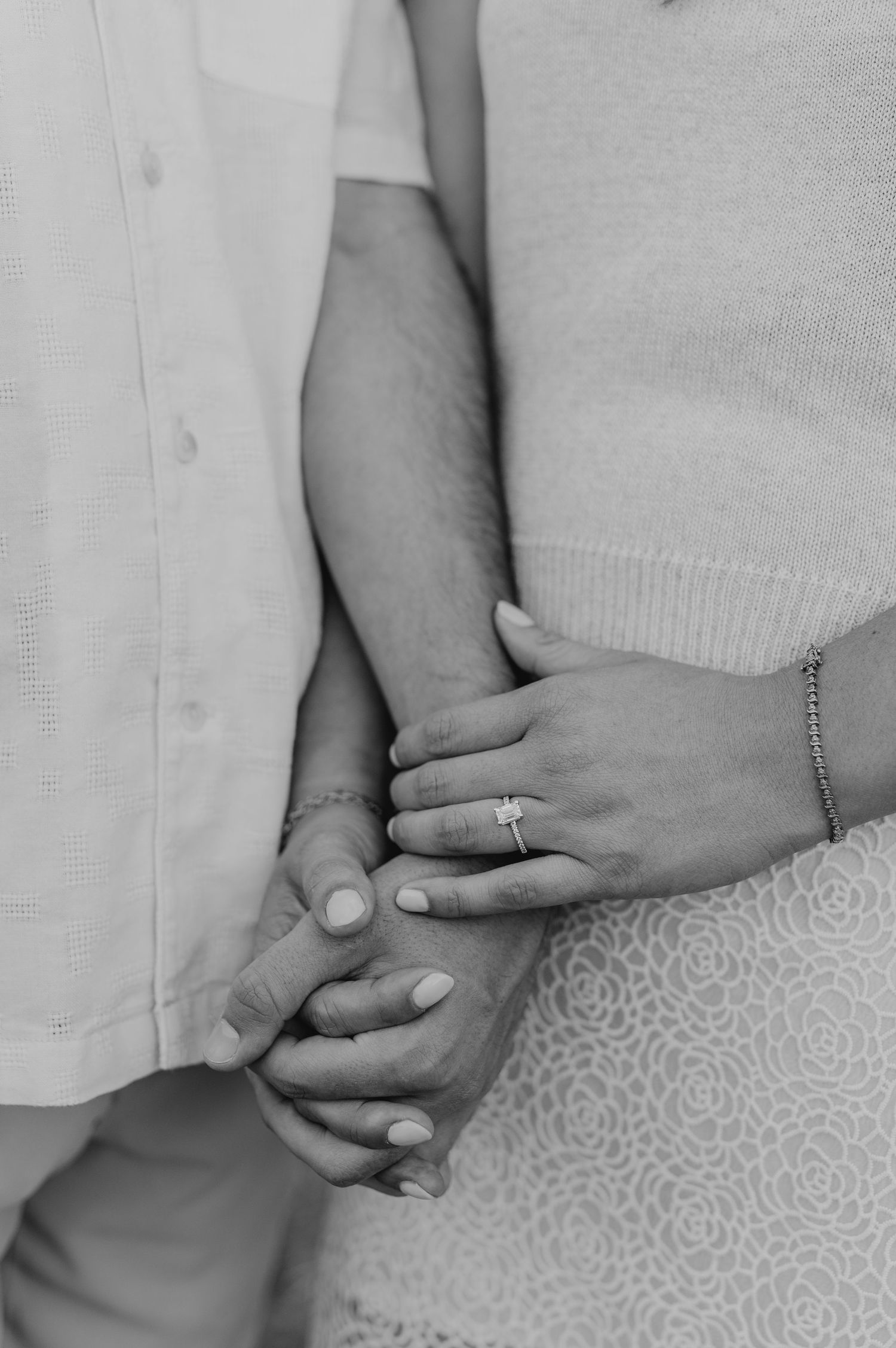 Close-up black and white photo of hands holding together intimately with a wedding ring visible.
