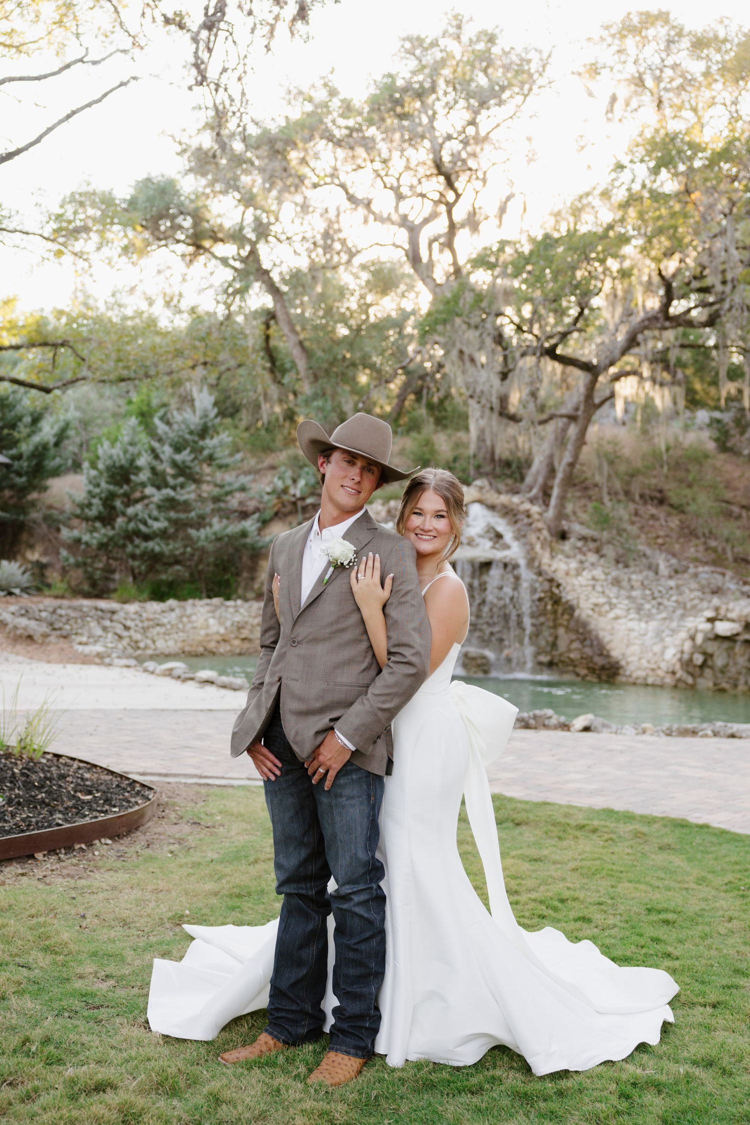 A couple poses for wedding portraits in front of a rustic stone wall and moss-covered trees.