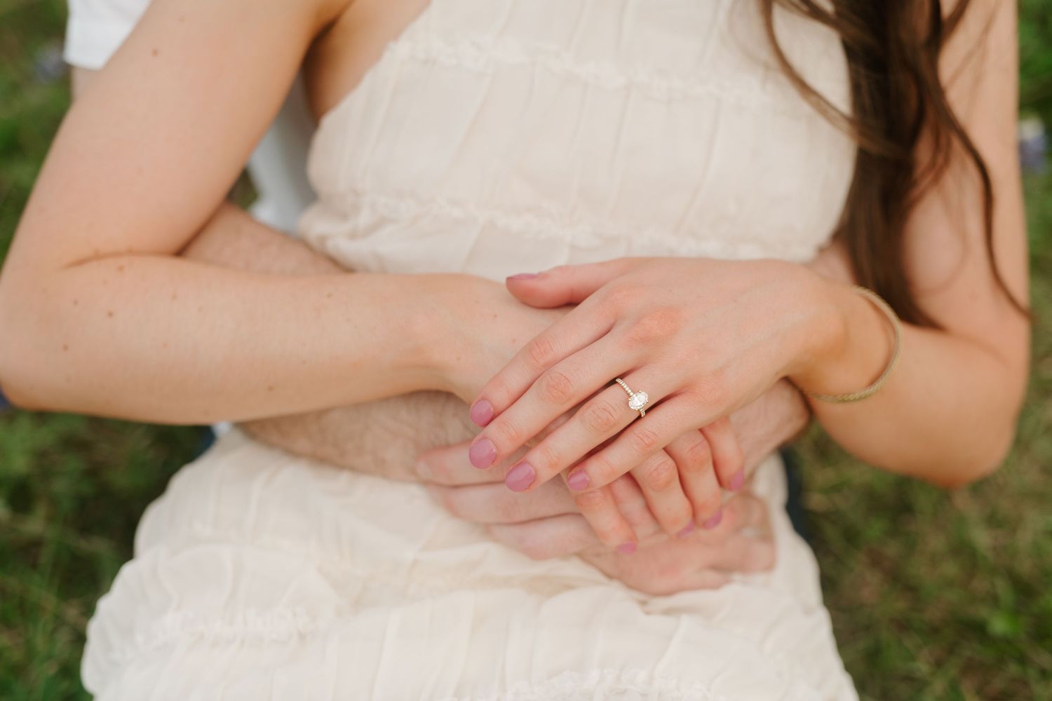 Close-up view of hands clasped together against a white lace dress in an outdoor setting.