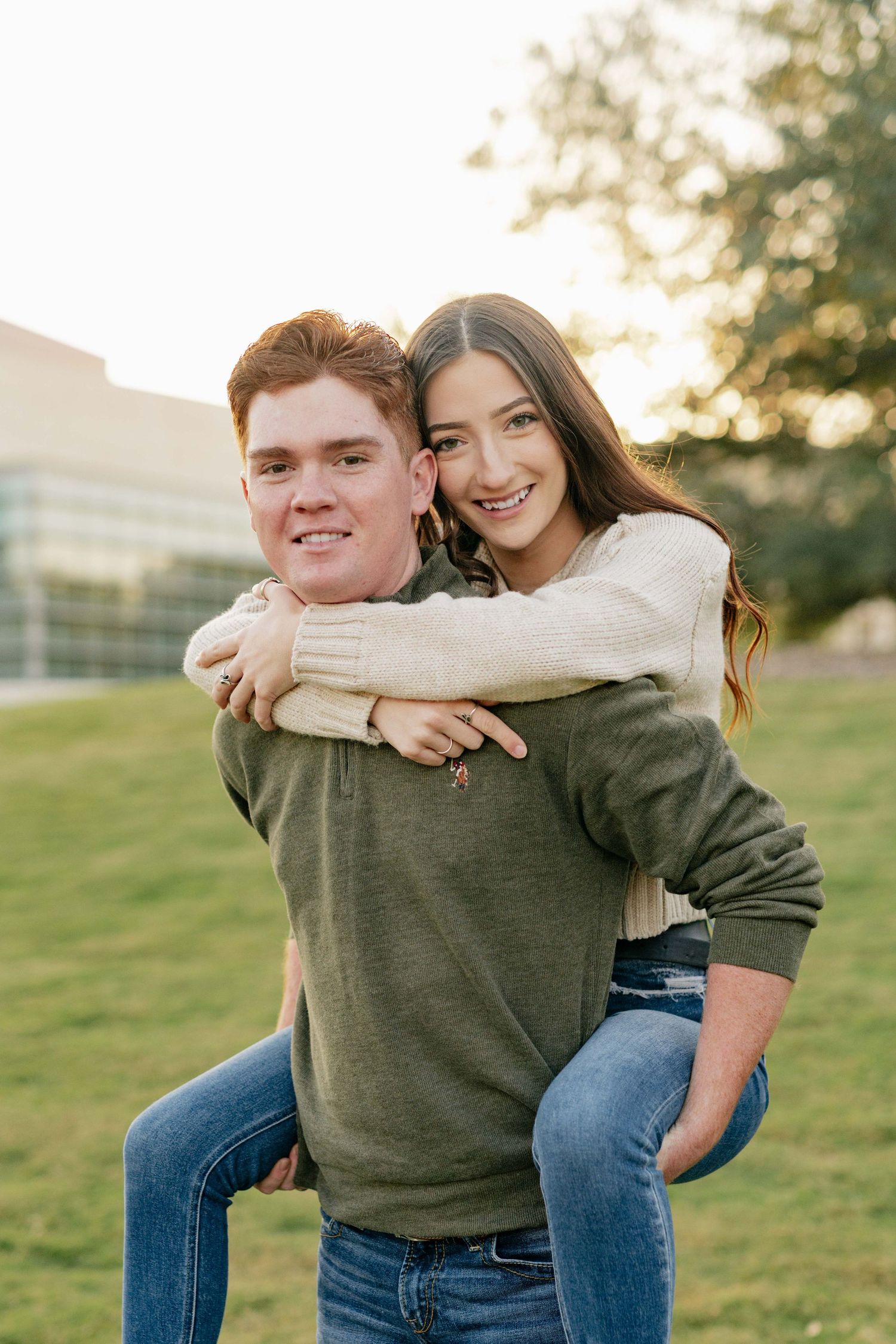 A playful piggyback ride moment between a couple on a grassy field at sunset.