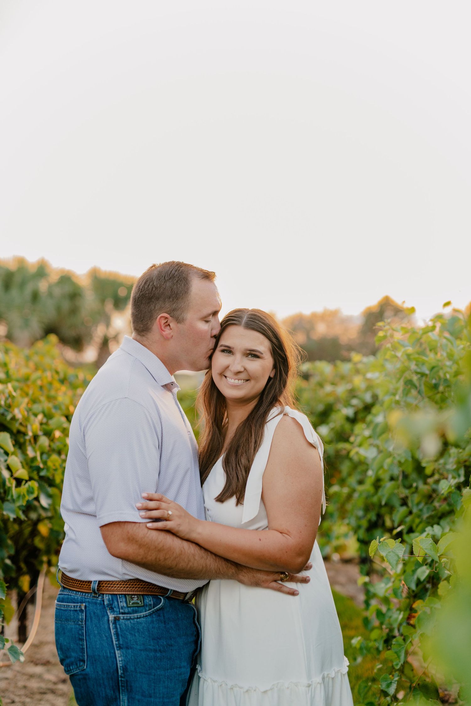 Couple sharing an intimate embrace among lush green grapevines during a vineyard photoshoot.