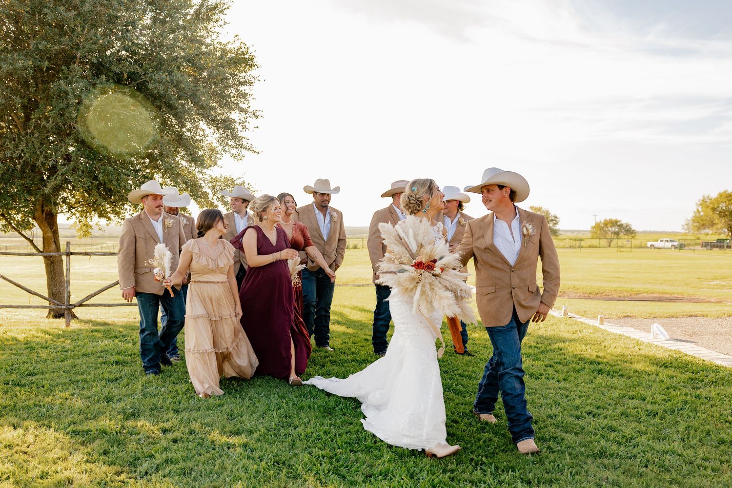 Wedding party in western attire posing outdoors on grassy field at sunset.