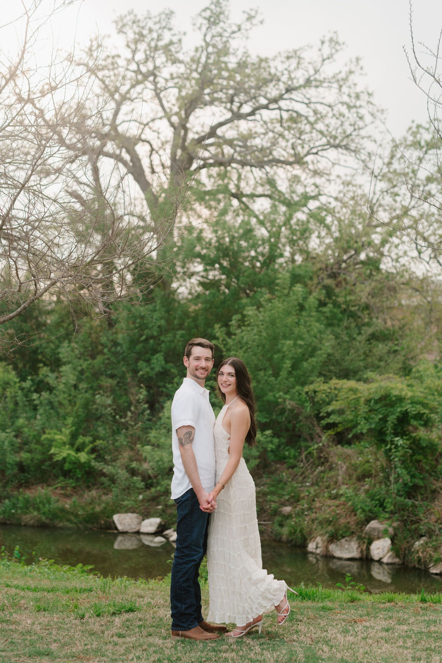 A couple poses together outdoors in a natural setting with trees and rocks in the background.