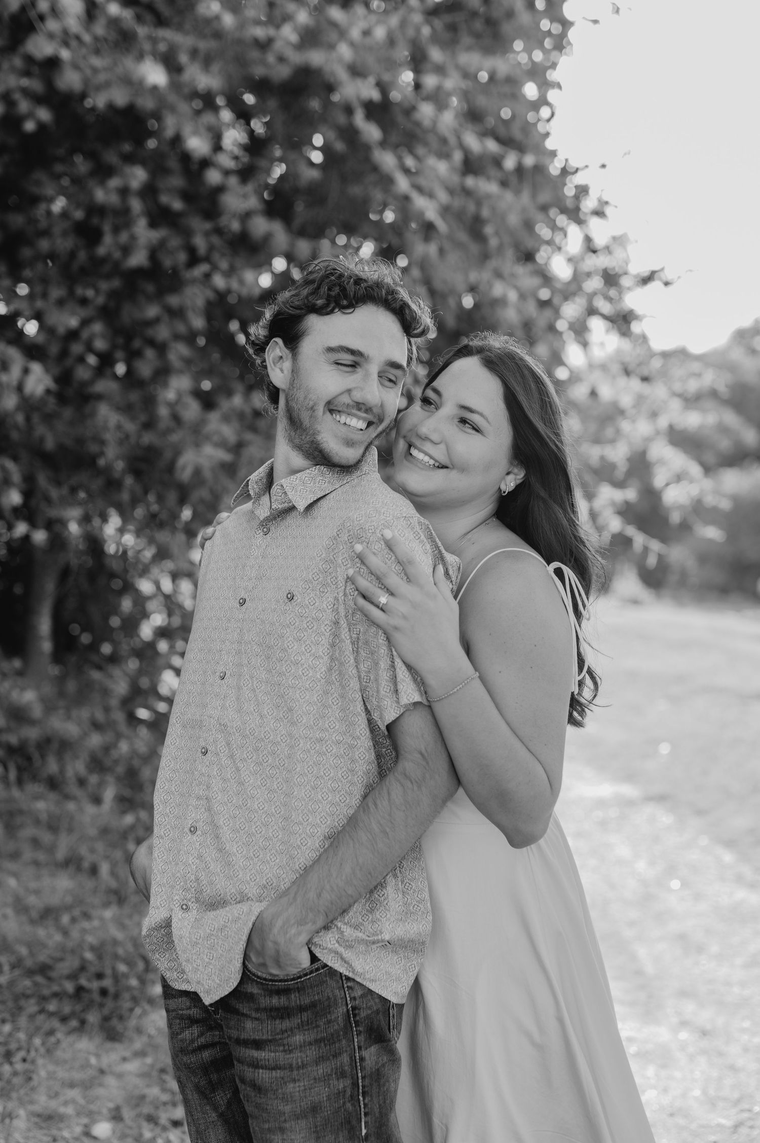 A black and white portrait captures a couple's joyful embrace in a natural setting.