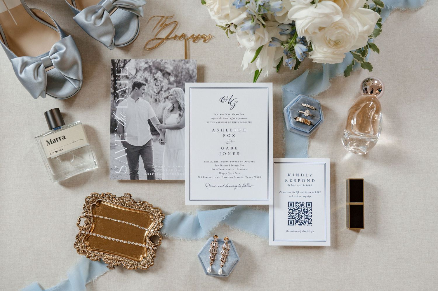 A flatlay of wedding accessories including a bridal bouquet, wedding invitation, and perfume bottles.