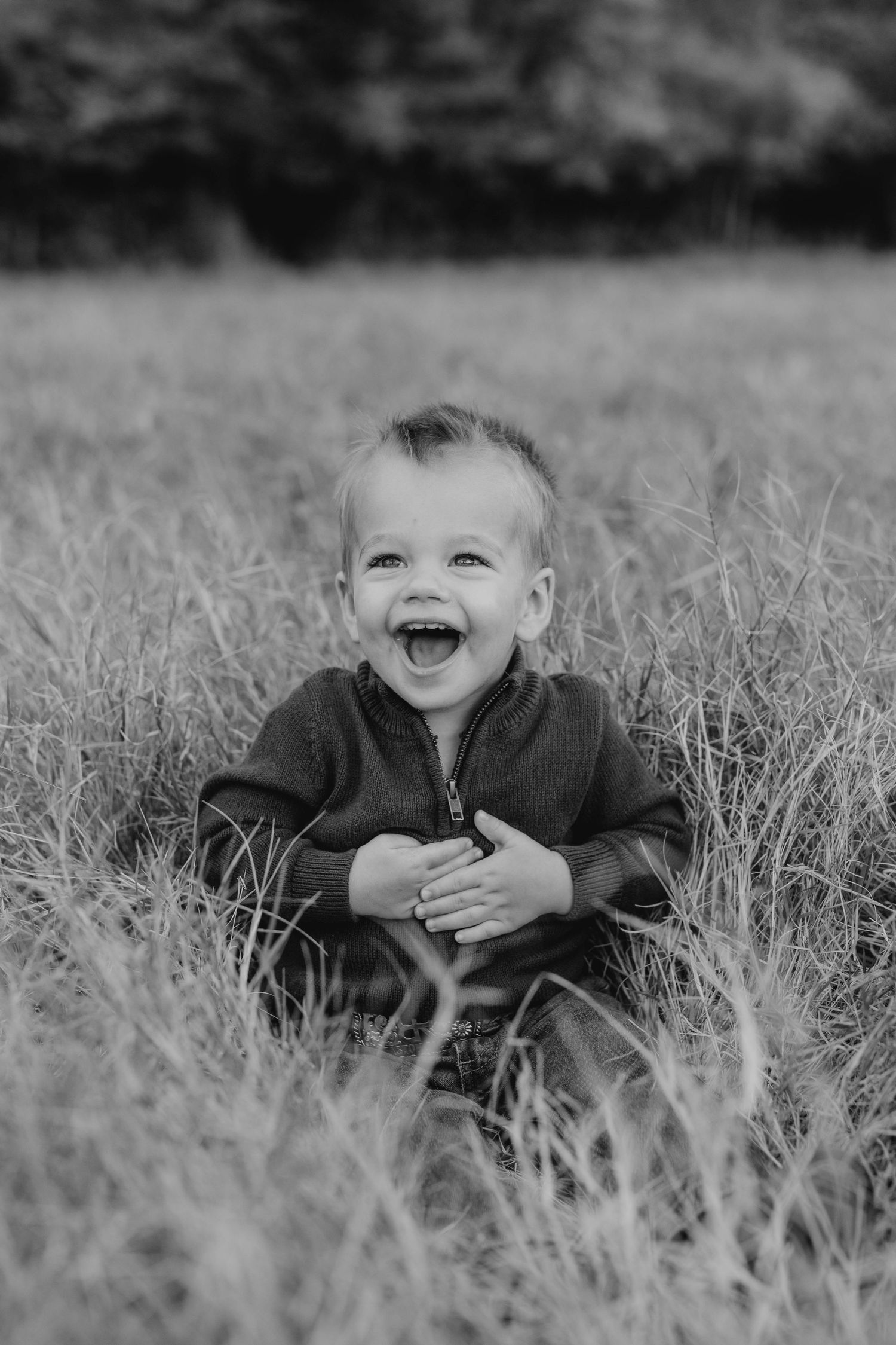 Black and white portrait of laughing child sitting in tall grass.