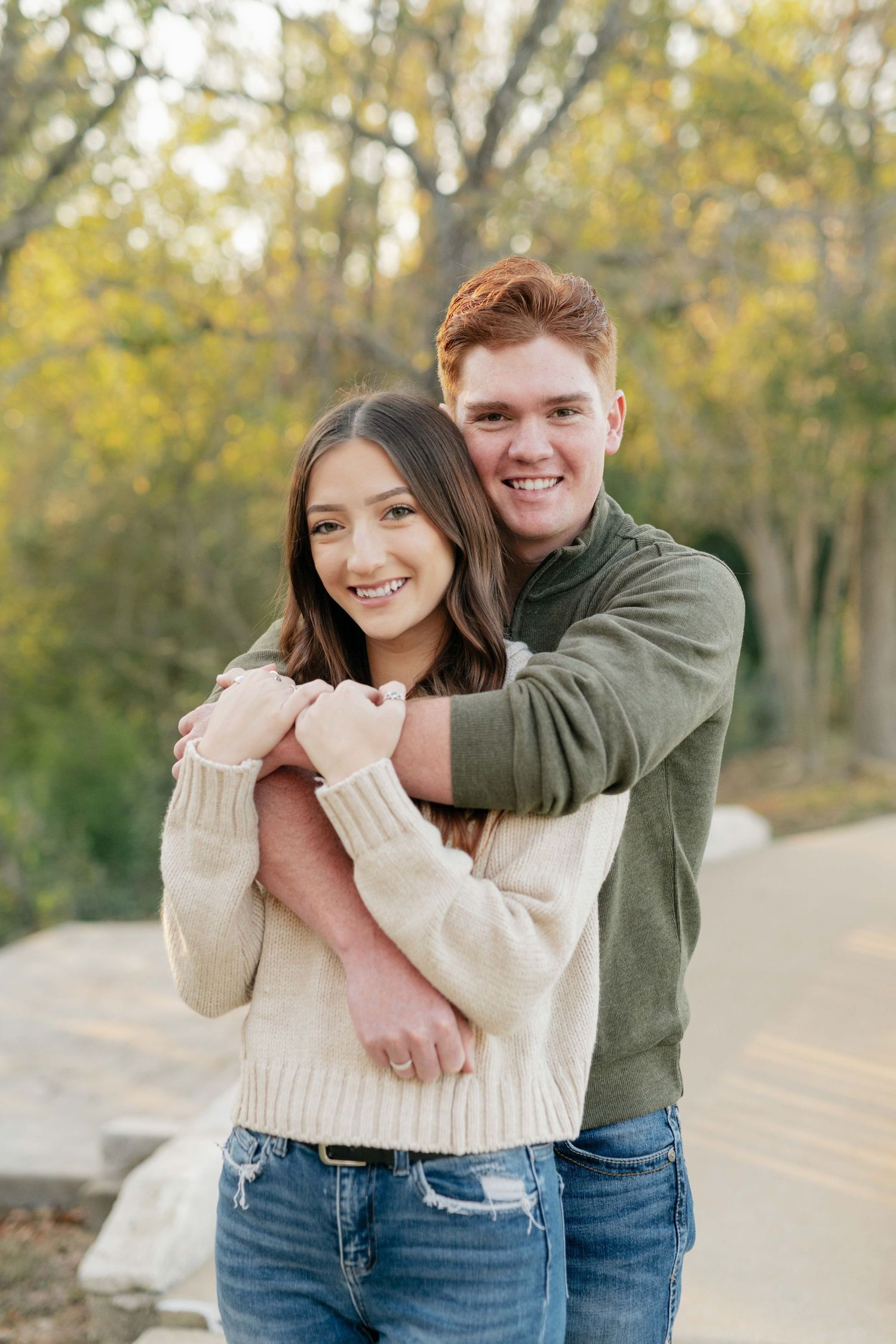 A romantic couple embraces outdoors while wearing casual sweaters against an autumn background.