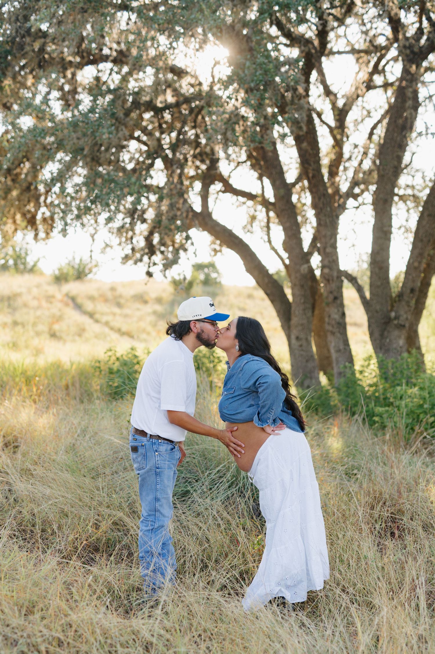 Romantic sequence of a couple walking and embracing in a sunlit field with oak trees in the background.