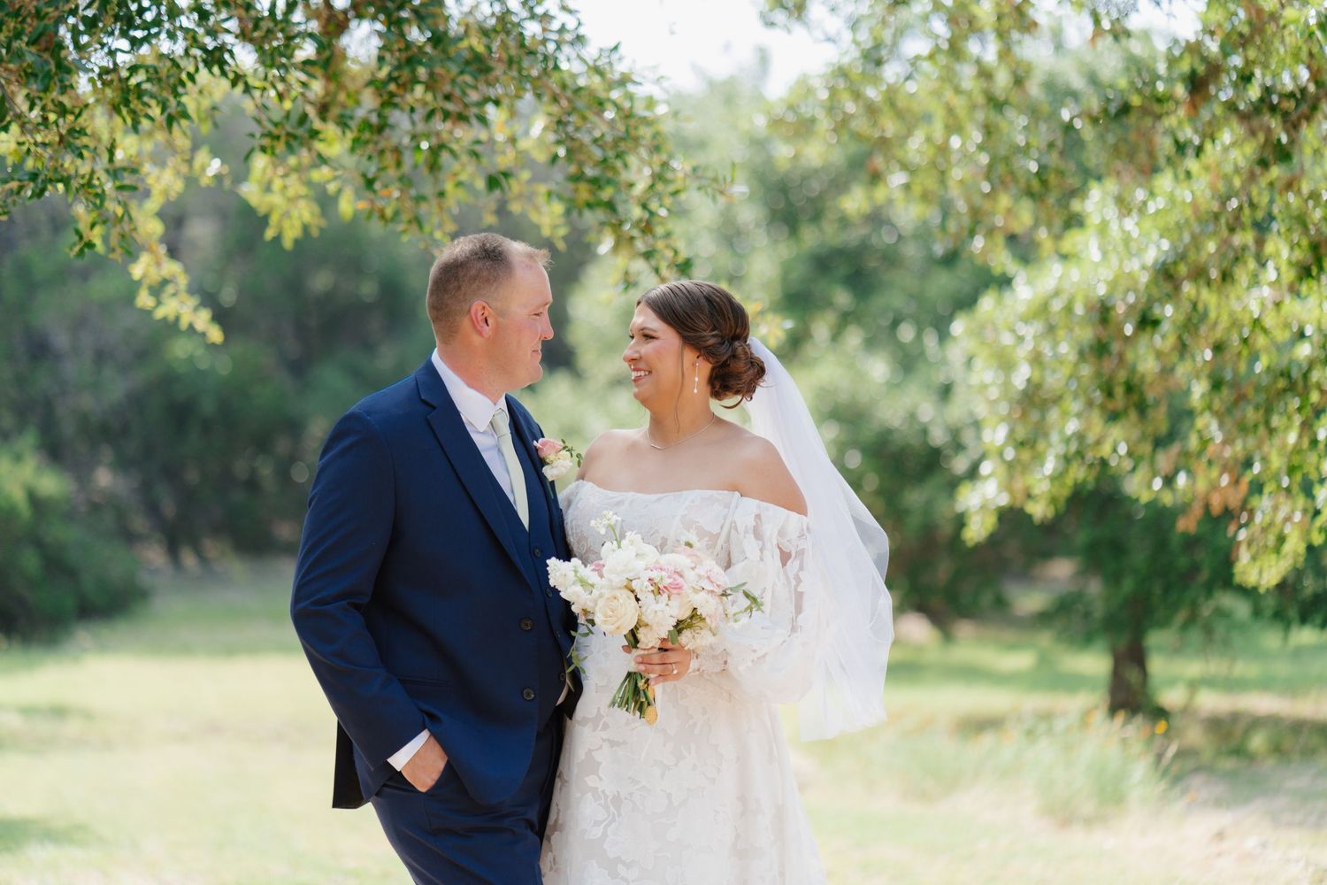 A romantic outdoor wedding portrait captured among blooming trees and natural greenery.