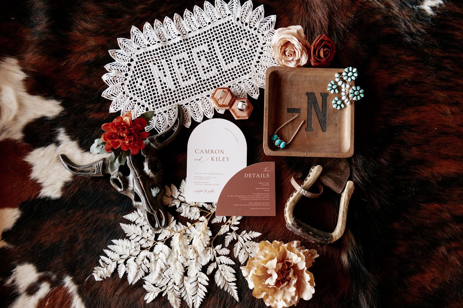 Wedding invitation suite with dried flowers, 'HELL' sign, and leather notebook on dark fur background.