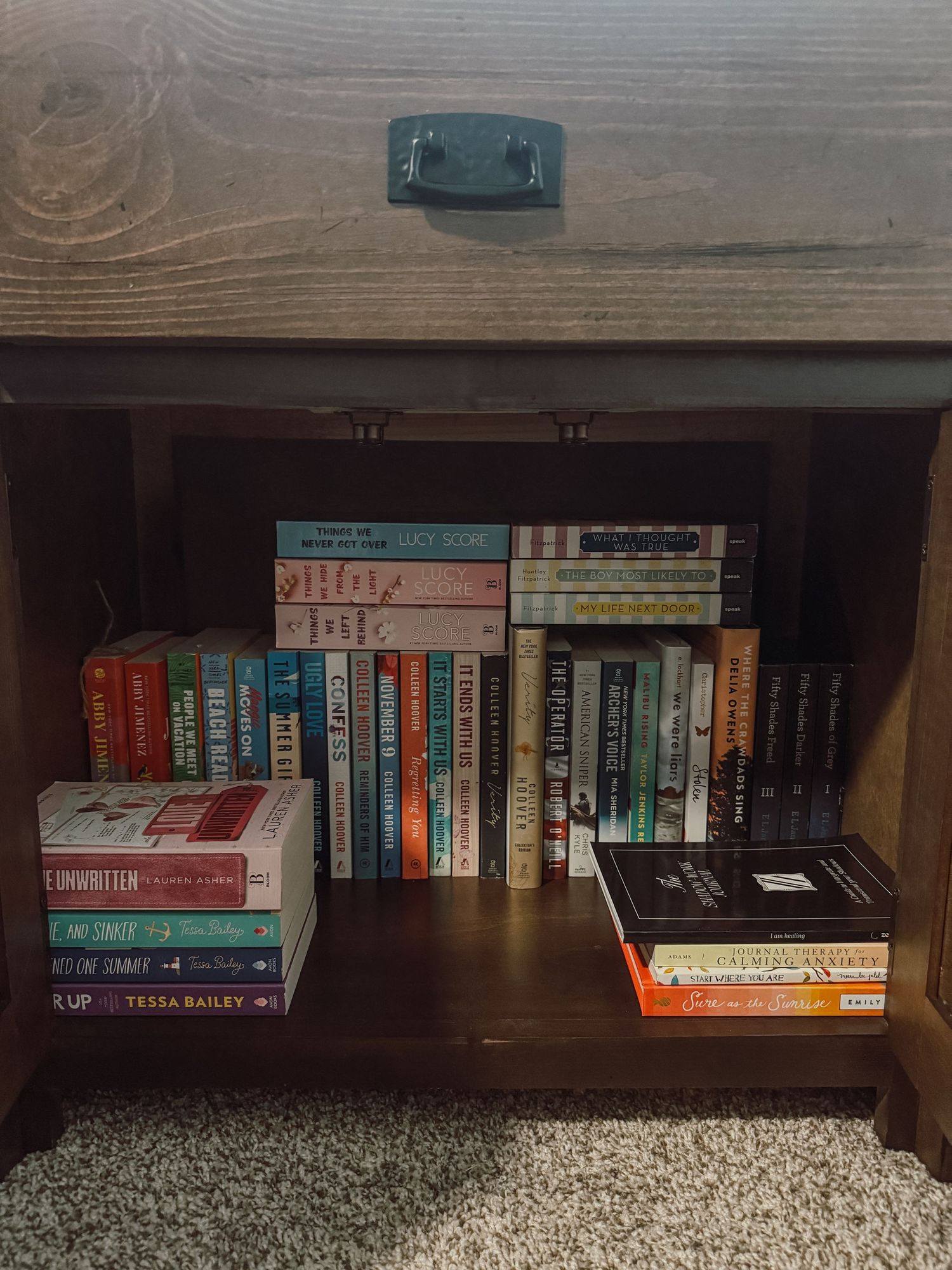 A wooden bookshelf displays a collection of colorful hardcover and paperback books arranged horizontally on multiple shelves.