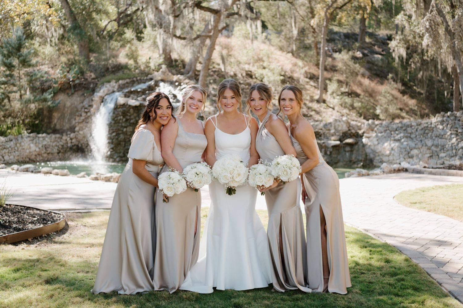 Wedding party members in coordinated gray dresses standing together outdoors.