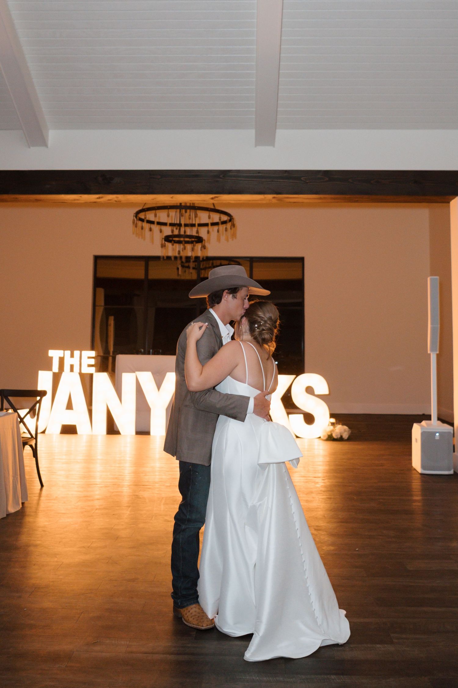 Wedding couple dances in front of illuminated marquee letters in a reception venue.