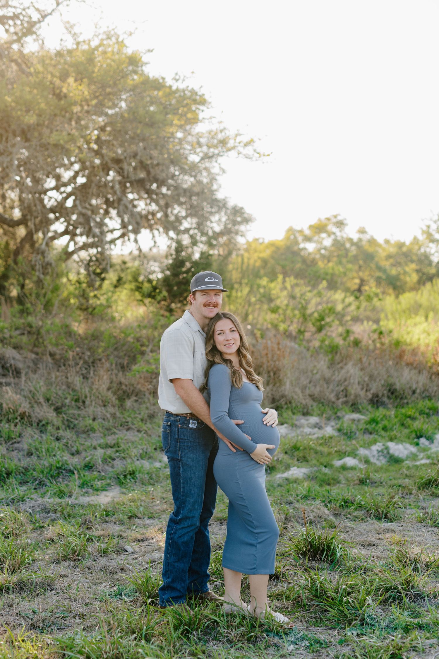 Couple poses together outdoors in a natural setting during a maternity photoshoot at golden hour.