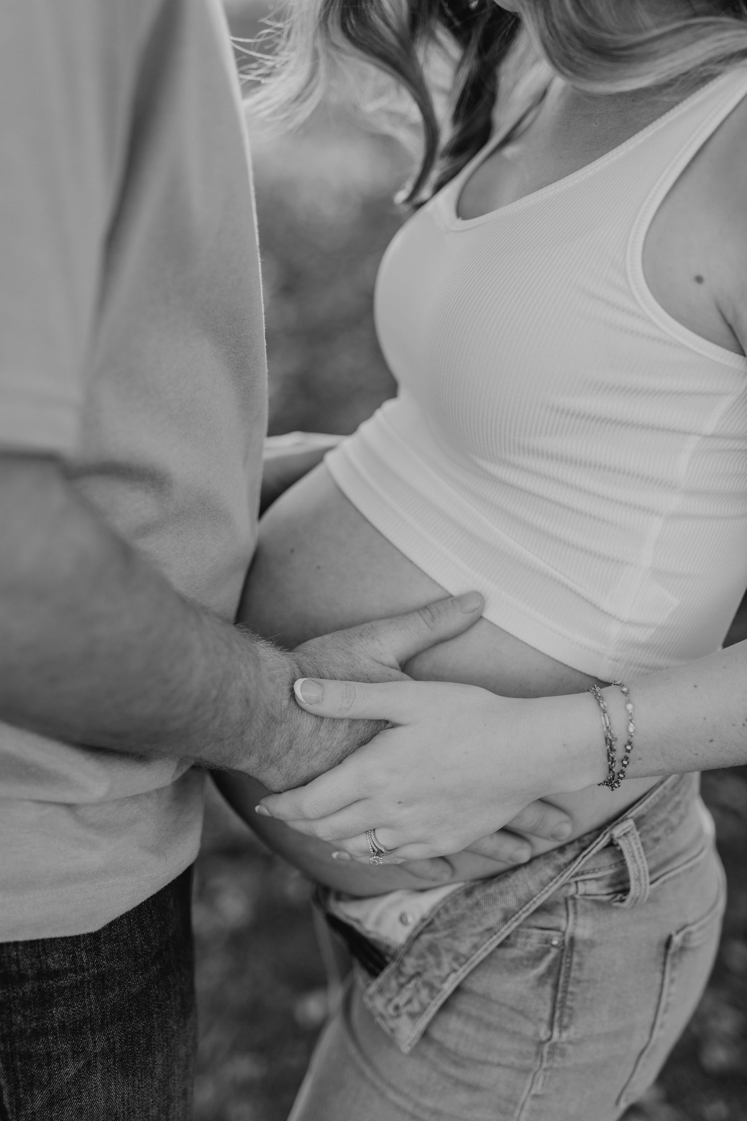 Intimate black and white close-up shows a couple's hands gently cradling a pregnant belly.