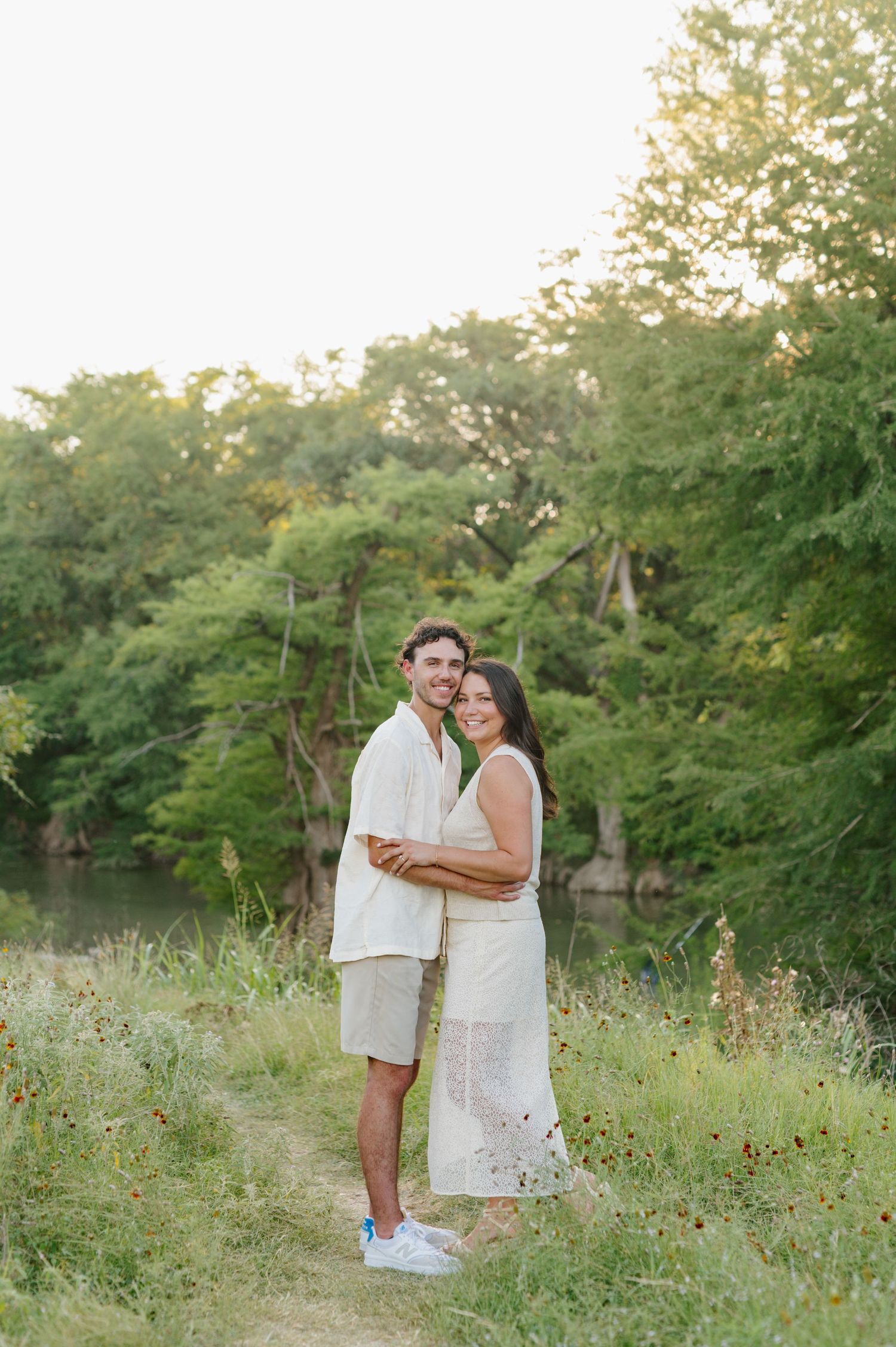 Couple in white outfits embracing in a wildflower field during golden hour.