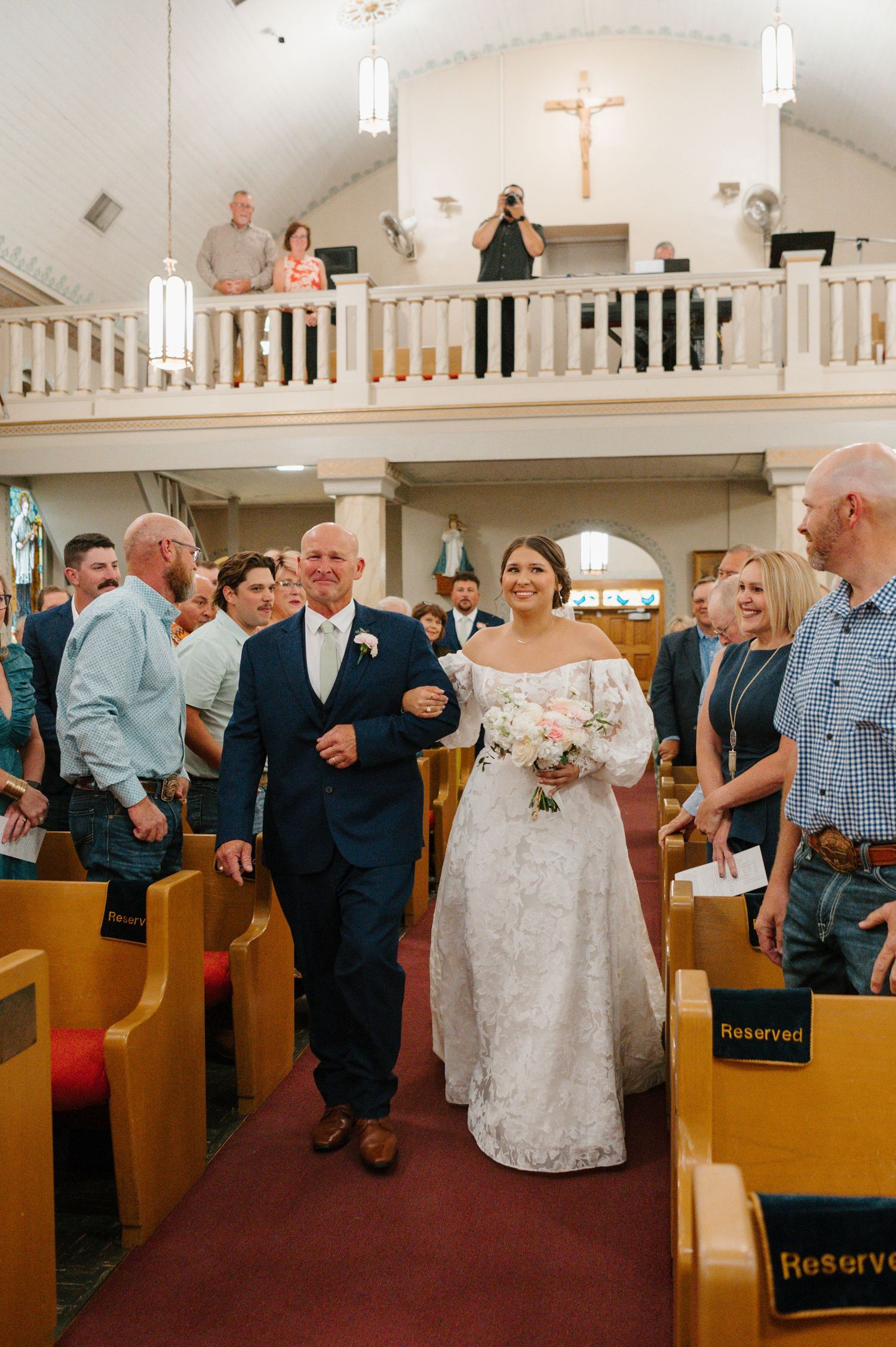 Wedding ceremony in a traditional church with wooden pews and a balcony overlooking the proceedings.