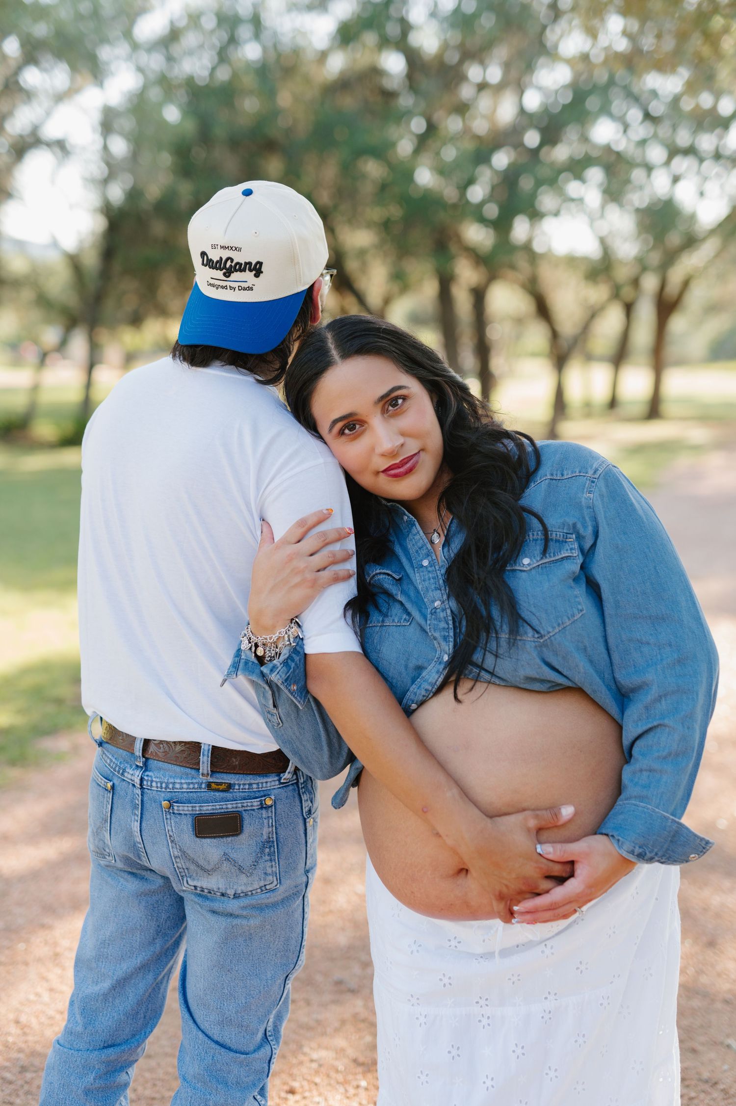 A couple in denim and white poses in a series of playful outdoor maternity photos.