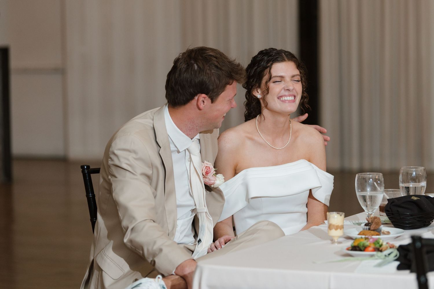 Wedding reception scene with couple and guests seated at dining tables in elegant indoor venue.