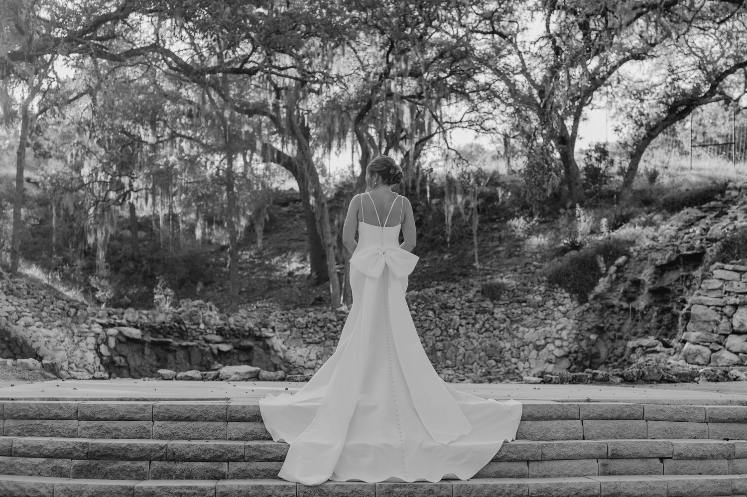 Black and white photo of a wedding dress flowing down stone garden steps with Spanish moss trees in background.
