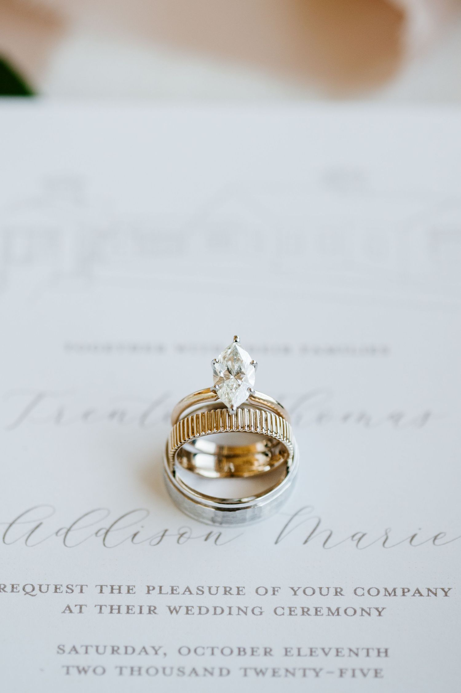 Wedding rings and invitation details photographed on white paper with elegant calligraphy.