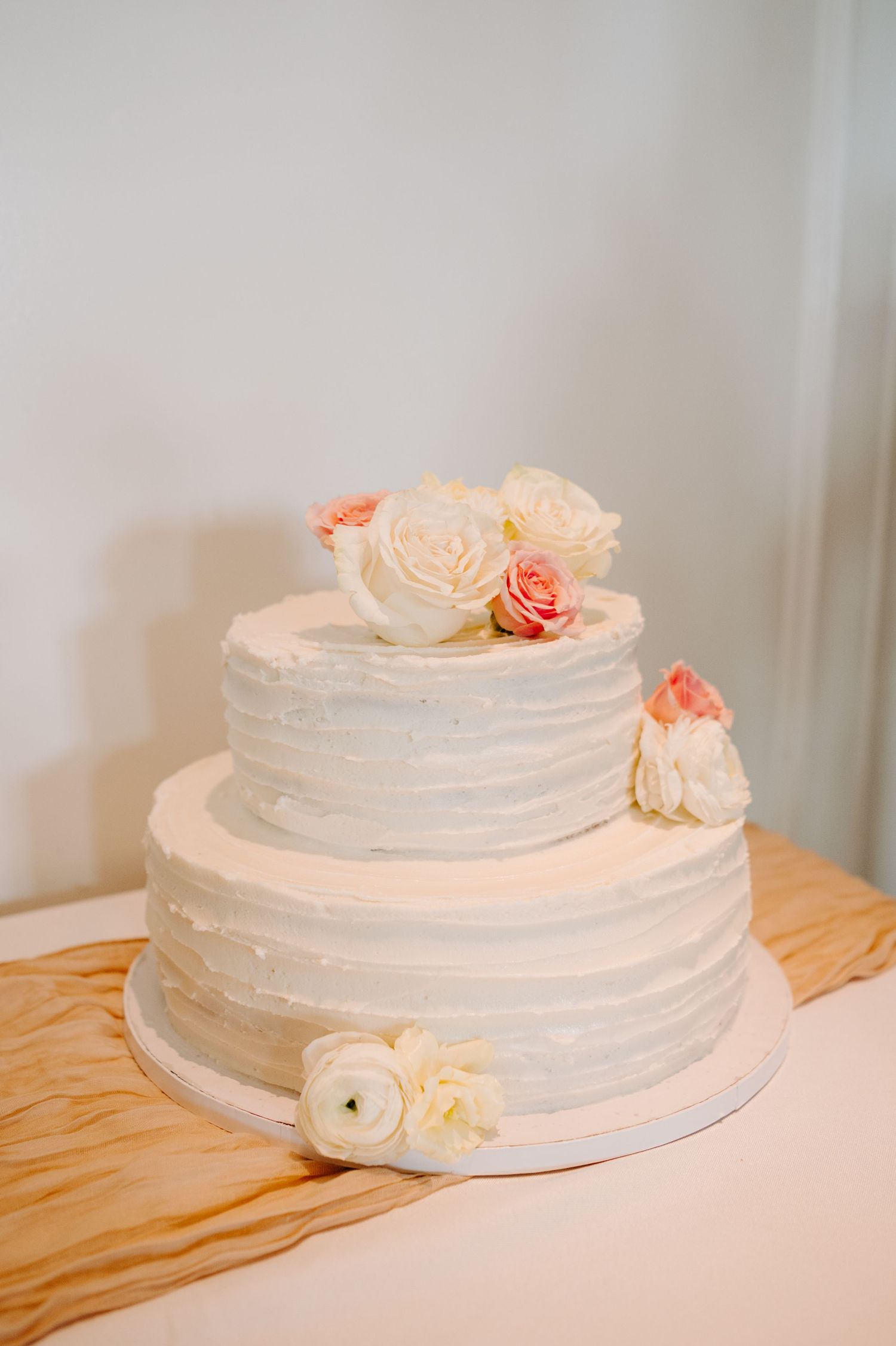 Elegant white tiered wedding cake decorated with fresh peach and cream roses.
