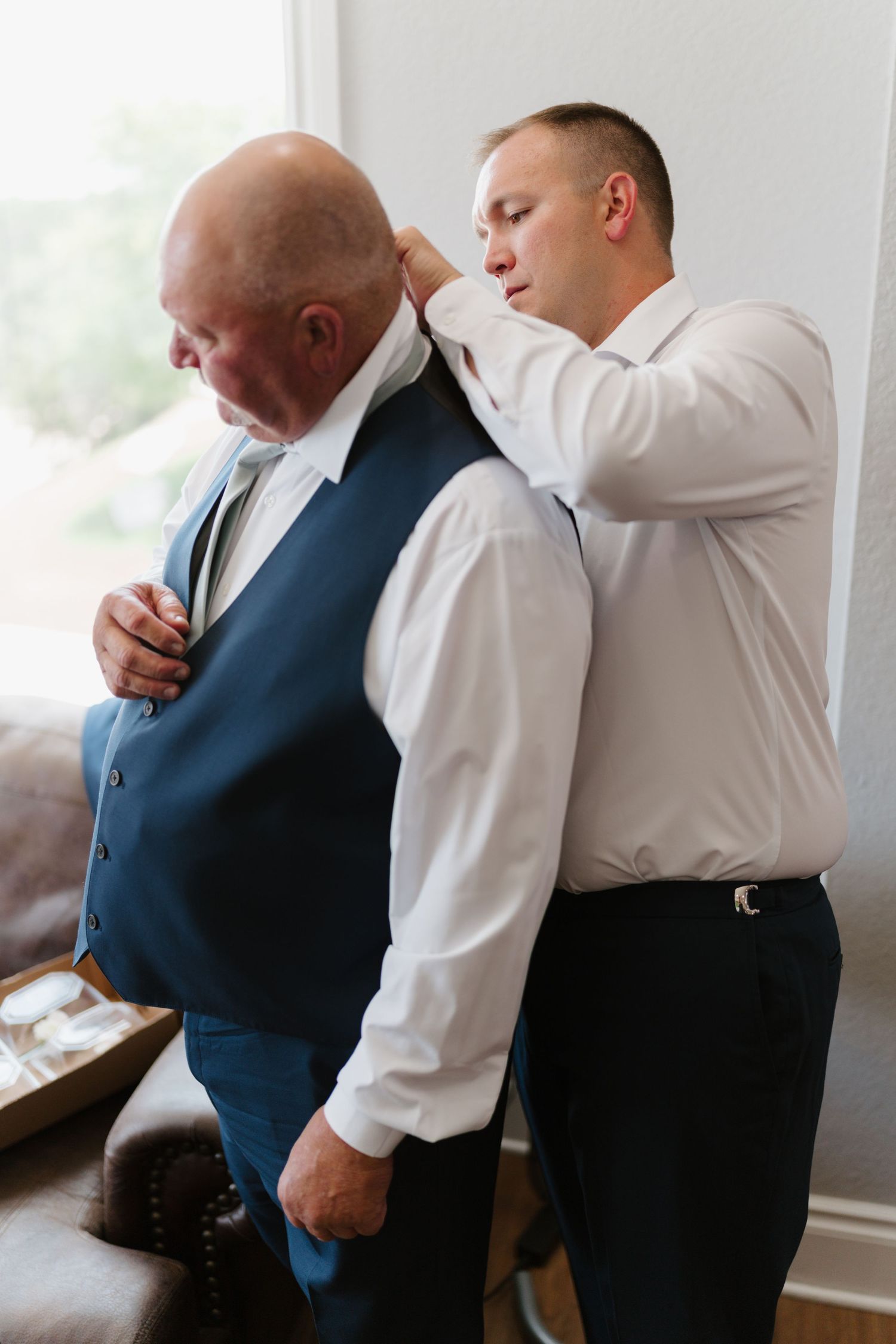 Groomsmen helping each other get ready in formal attire before the wedding ceremony.