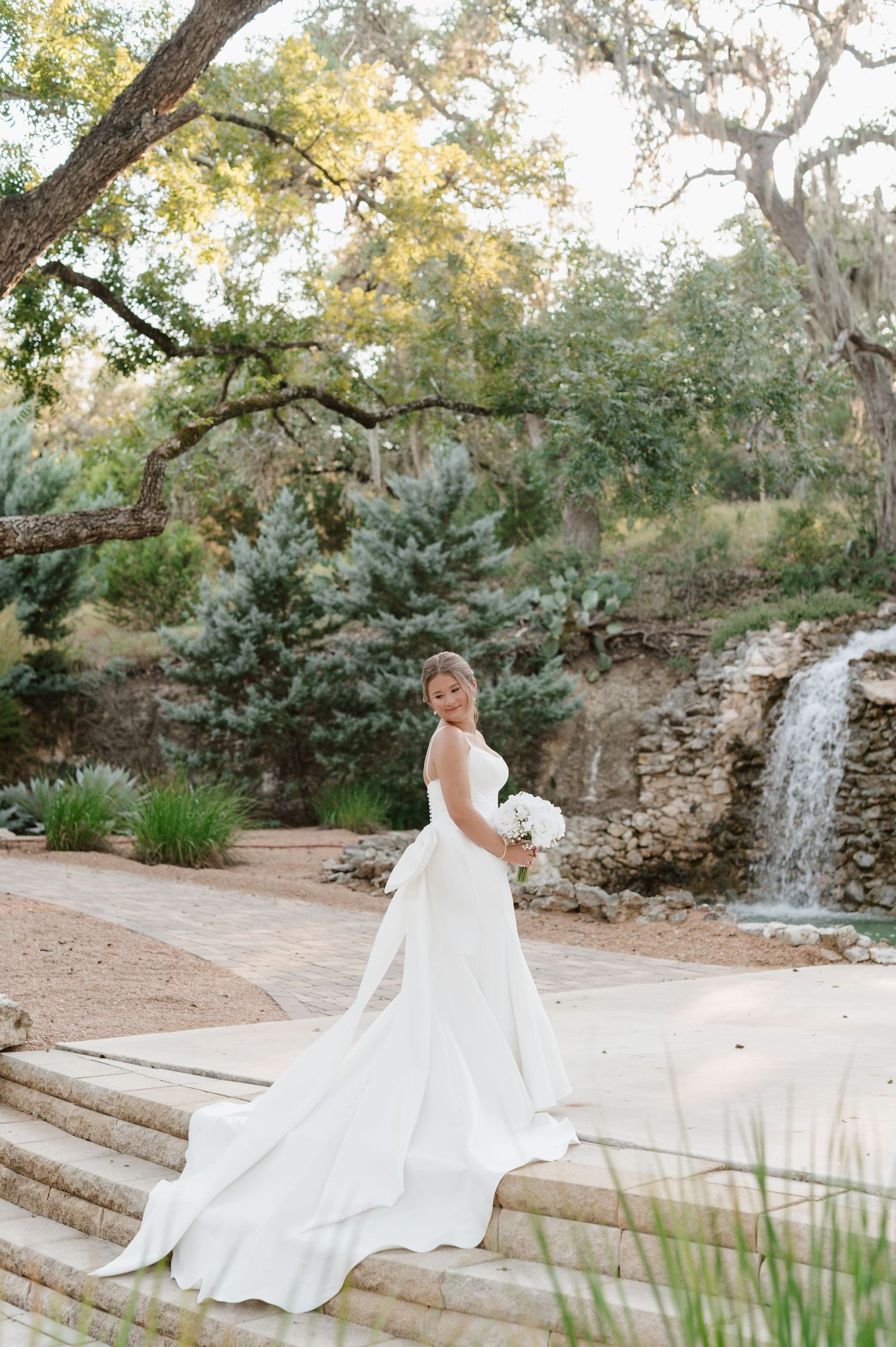 Elegant bridal photos taken in a garden setting with stone steps and a cascading waterfall feature.