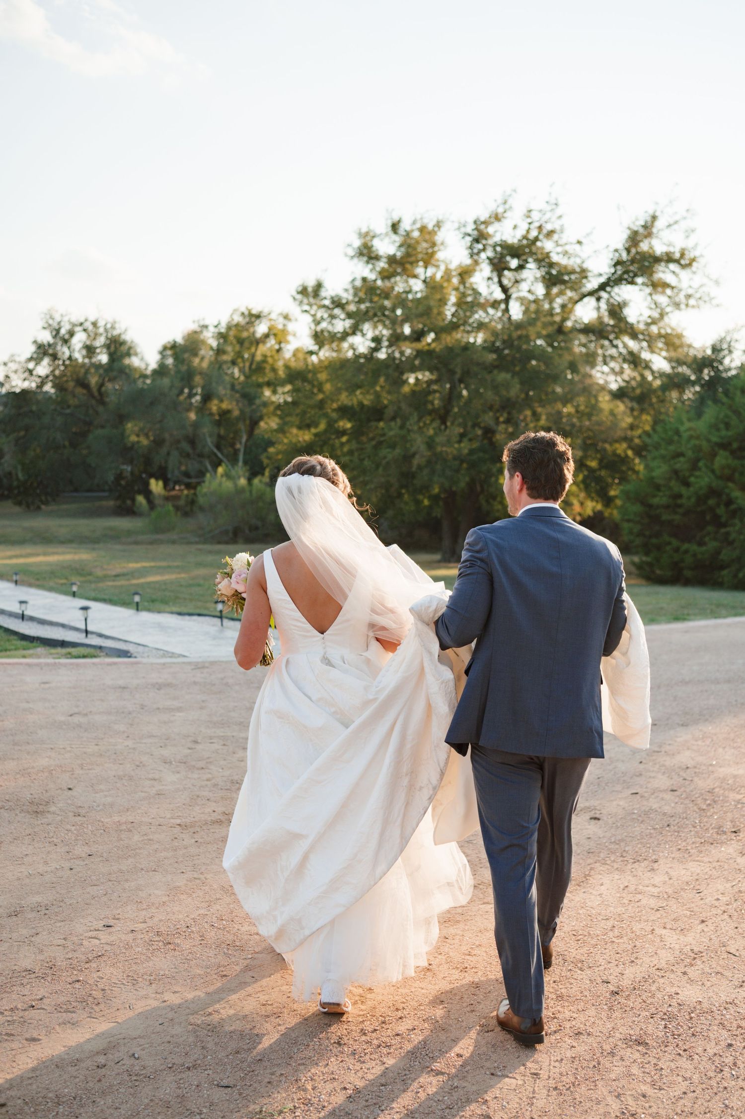 Newlywed couple walks together during golden hour sunset on a rustic outdoor path.