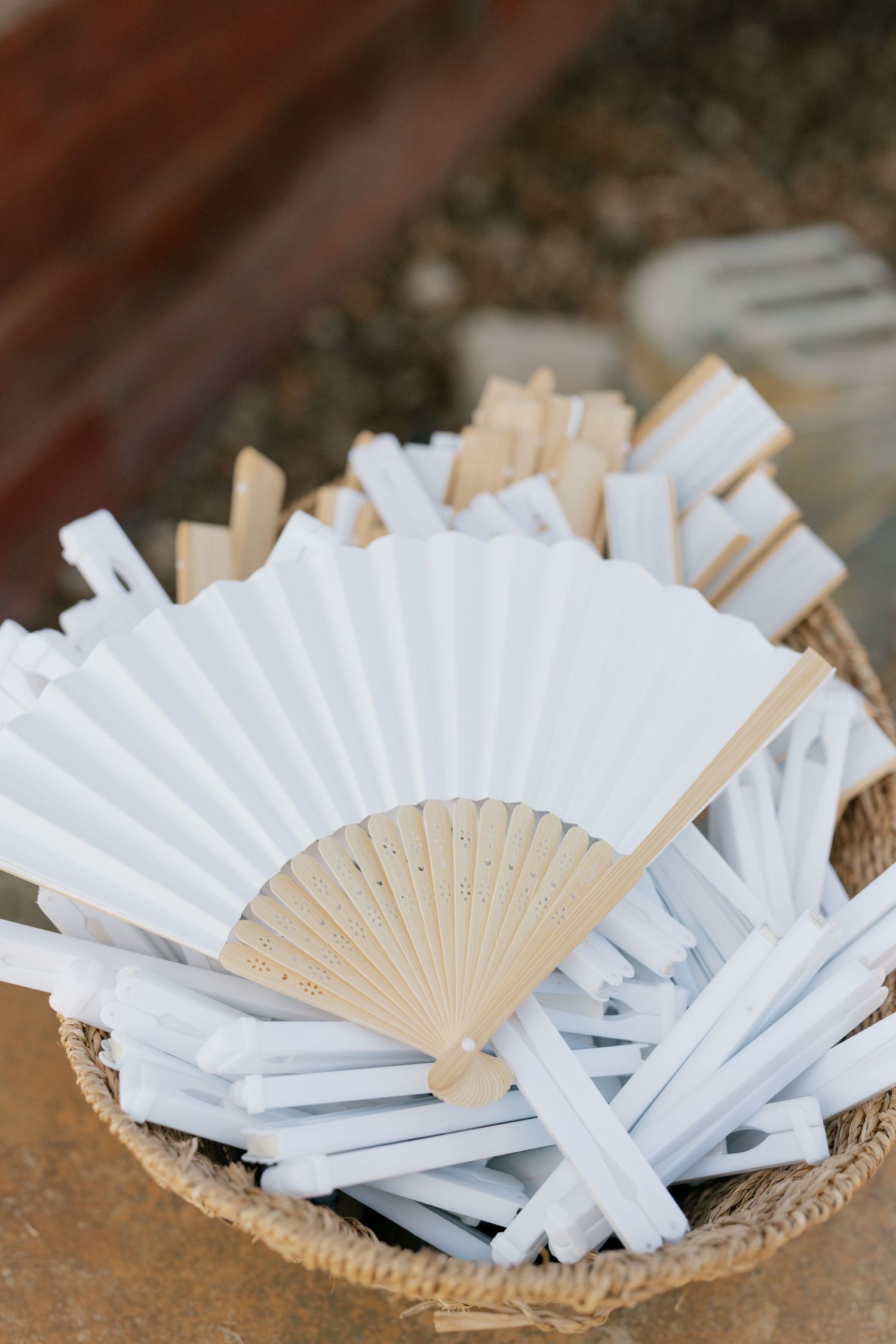 White paper fans arranged in woven basket for wedding guest favors.