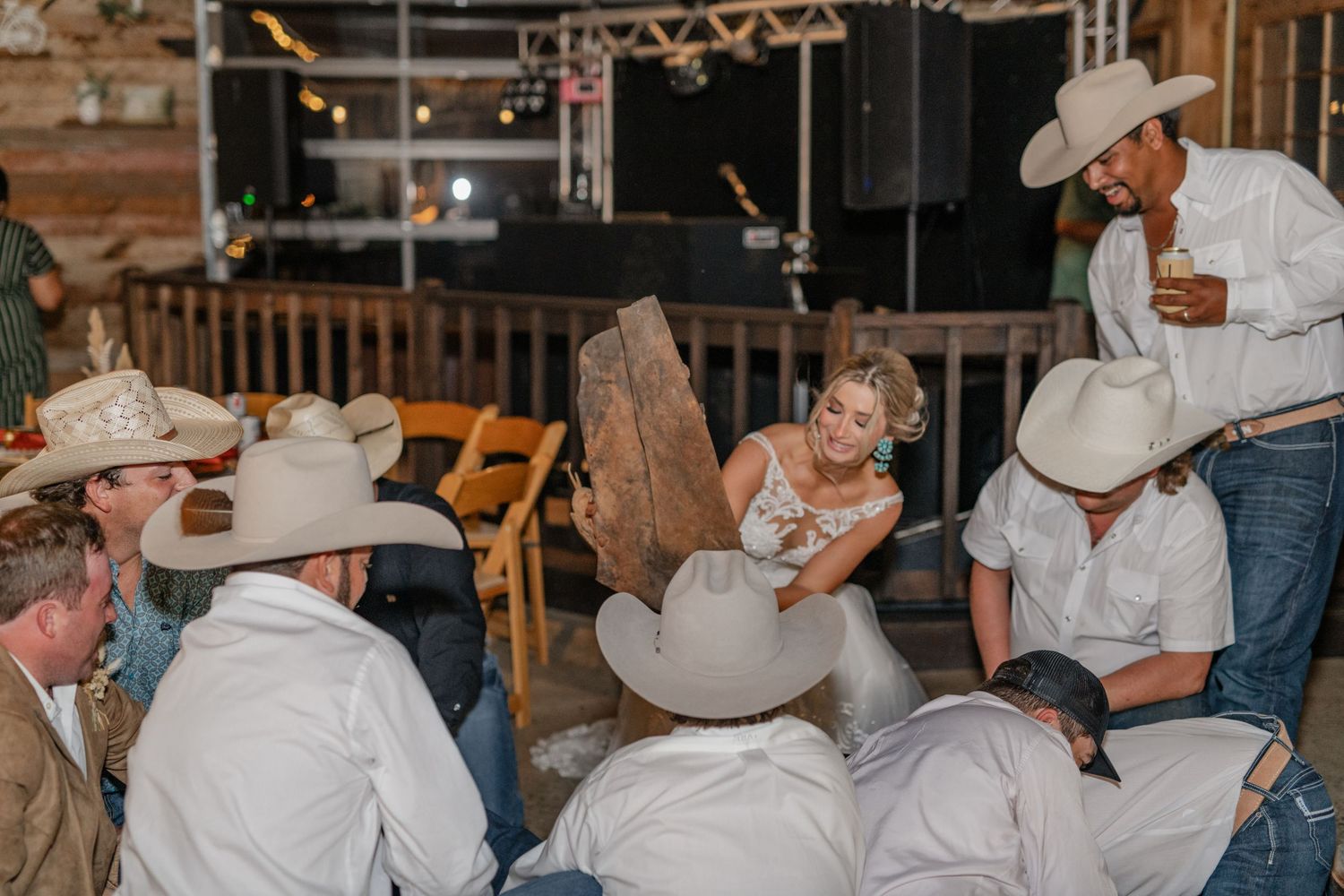 Wedding reception guests in cowboy hats gathered around tables at rustic indoor venue.