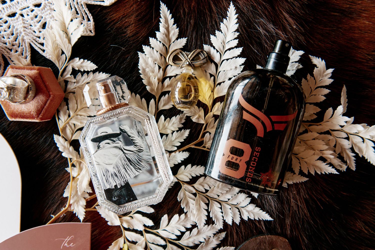 Glass perfume bottles and liquor arranged with silver ferns and lace on a dark surface.